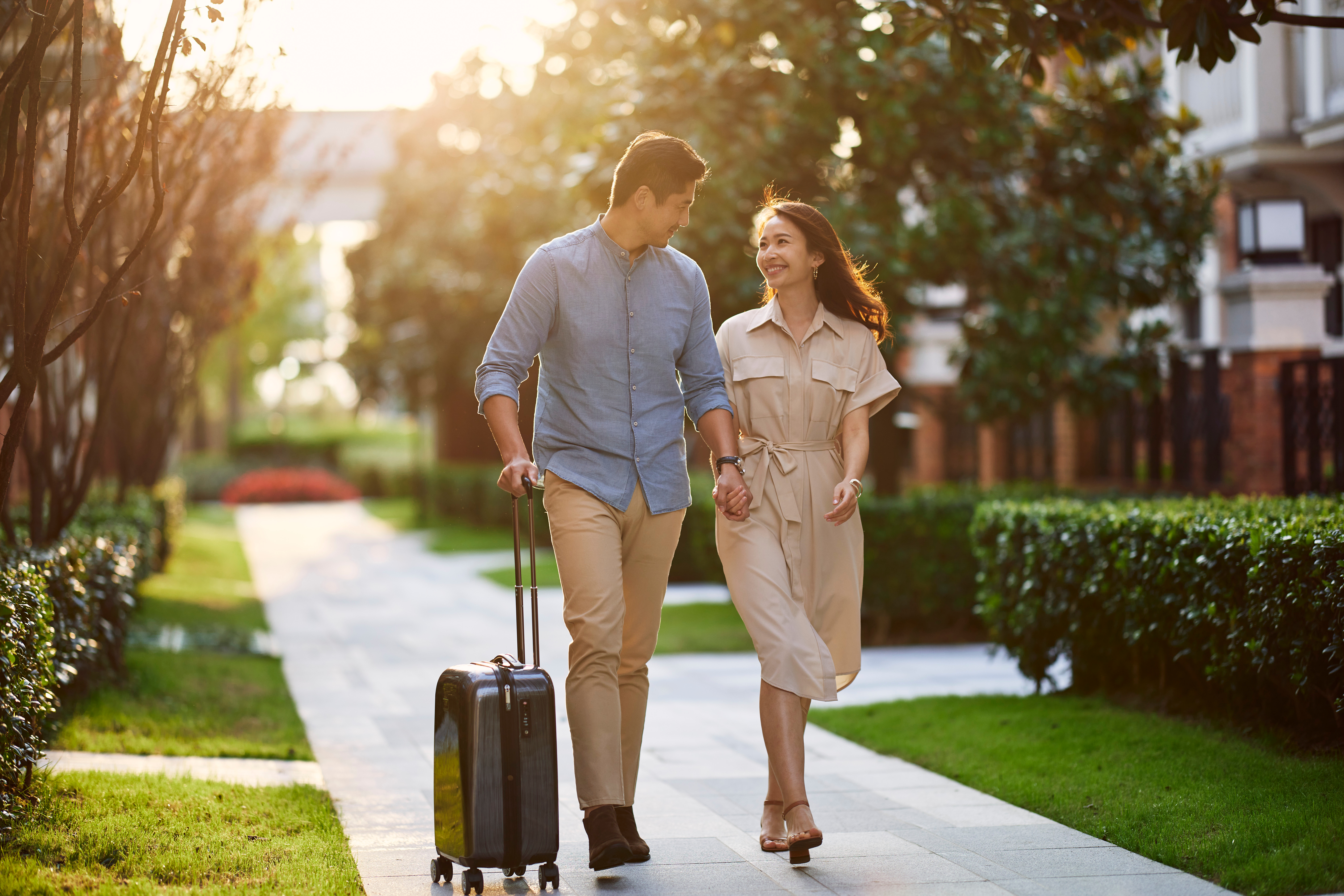 a man and woman holding hands and walking with luggage