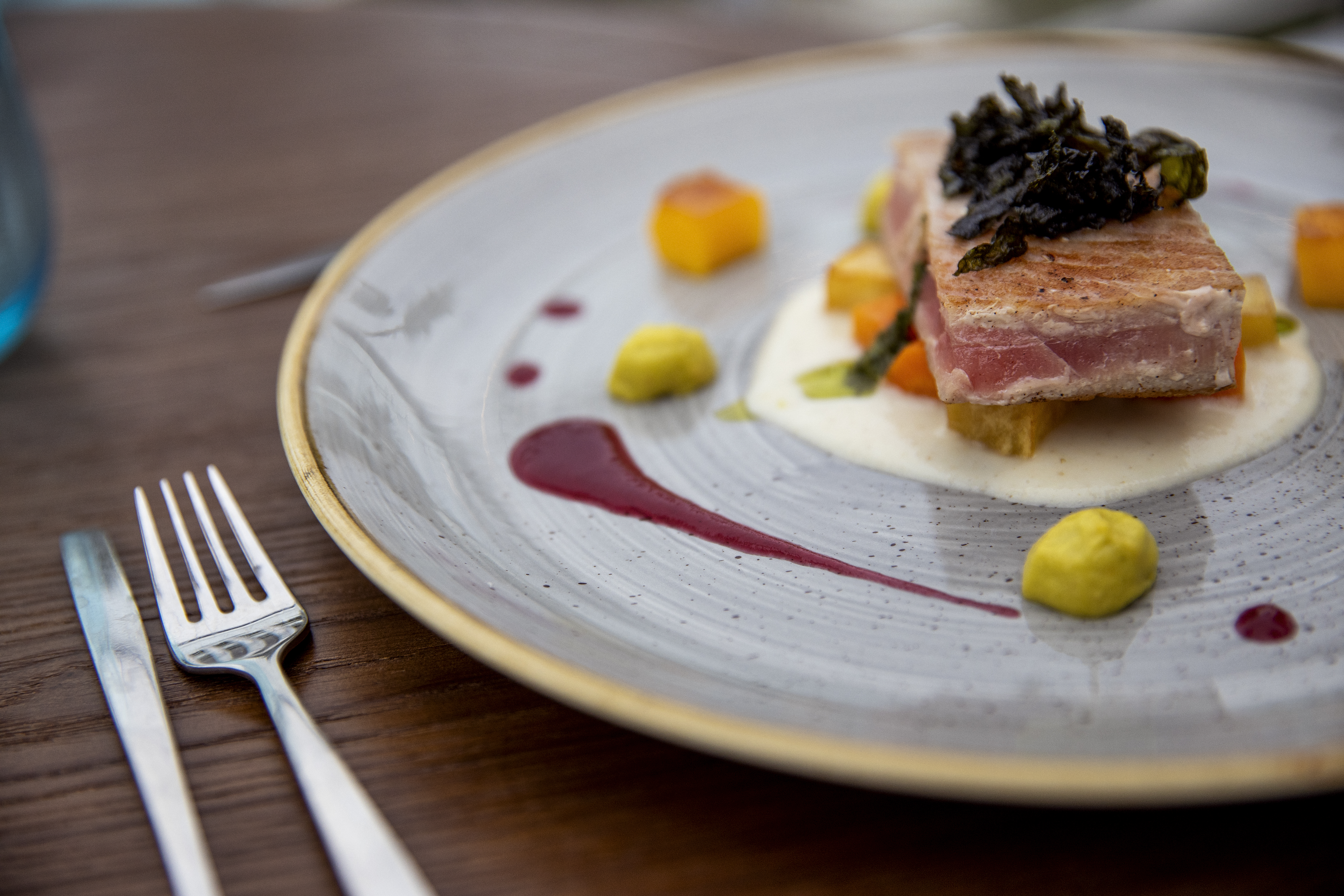 Gourmet seared tuna with dark topping, vegetables, and colorful sauces.