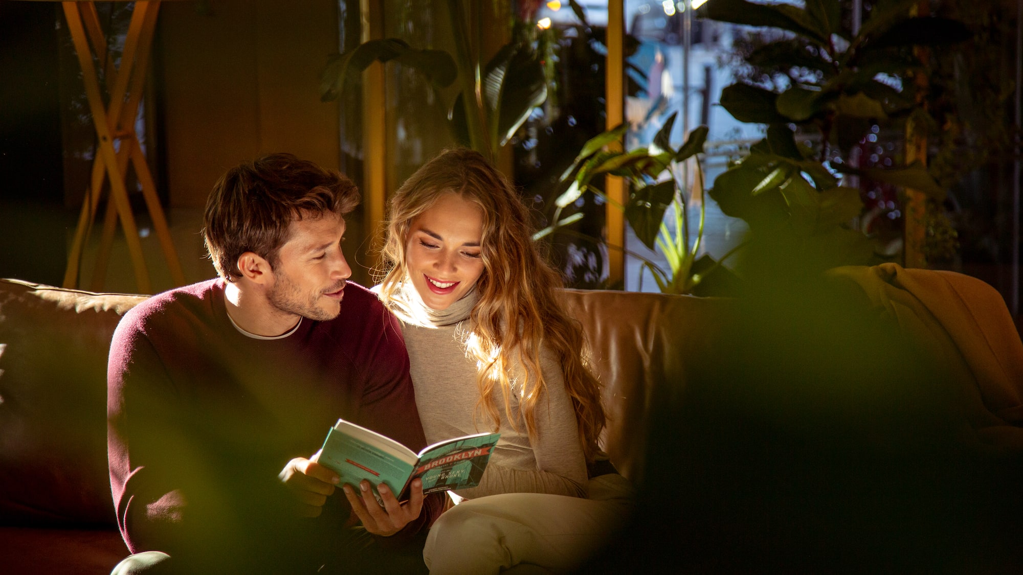 a man and woman sitting on a couch reading a book