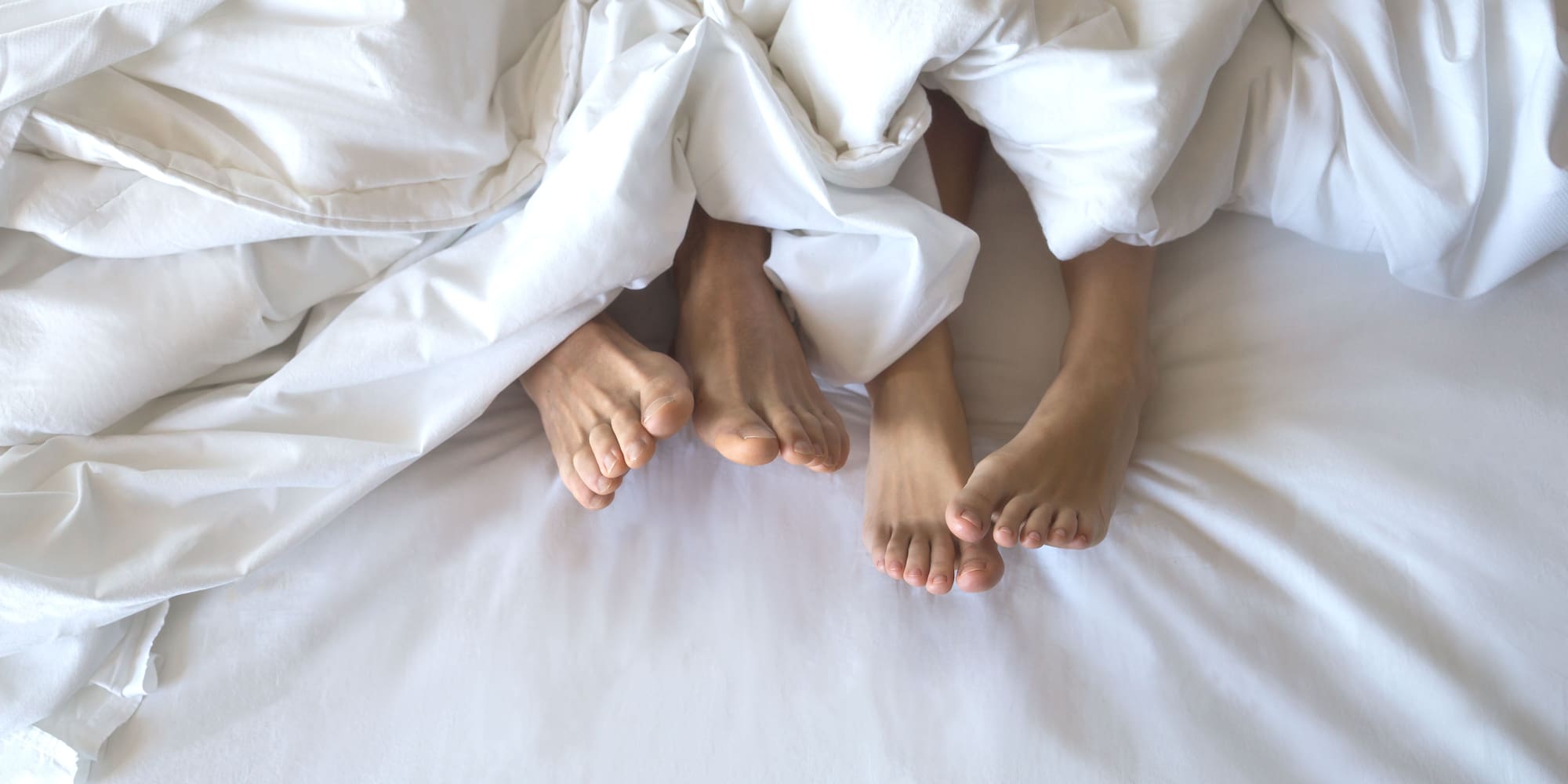 feet of a couple under a white blanket