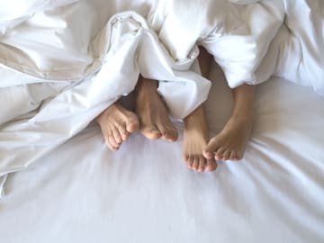 feet of a couple under a white blanket