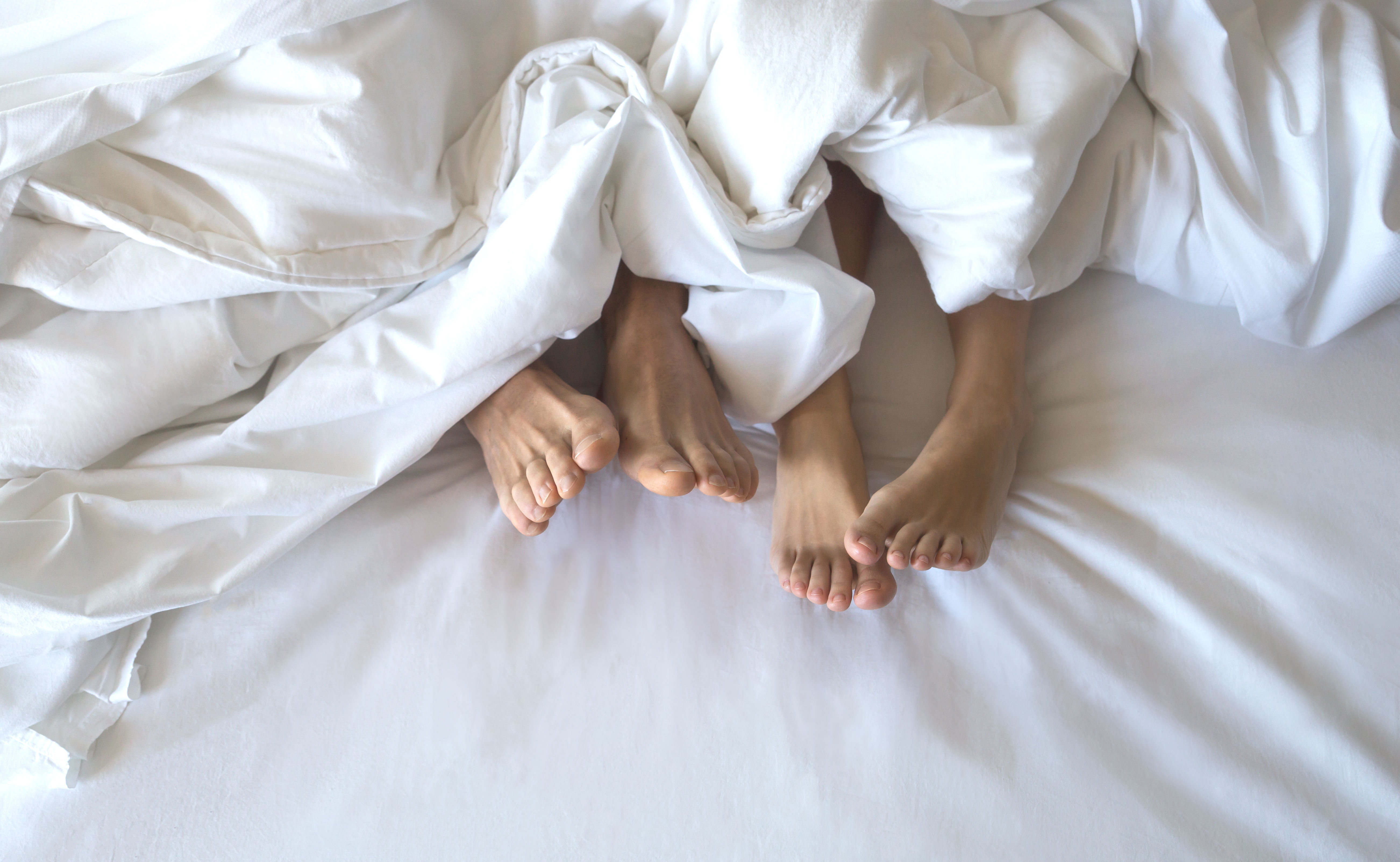 Bare feet of two people in white bed sheets.