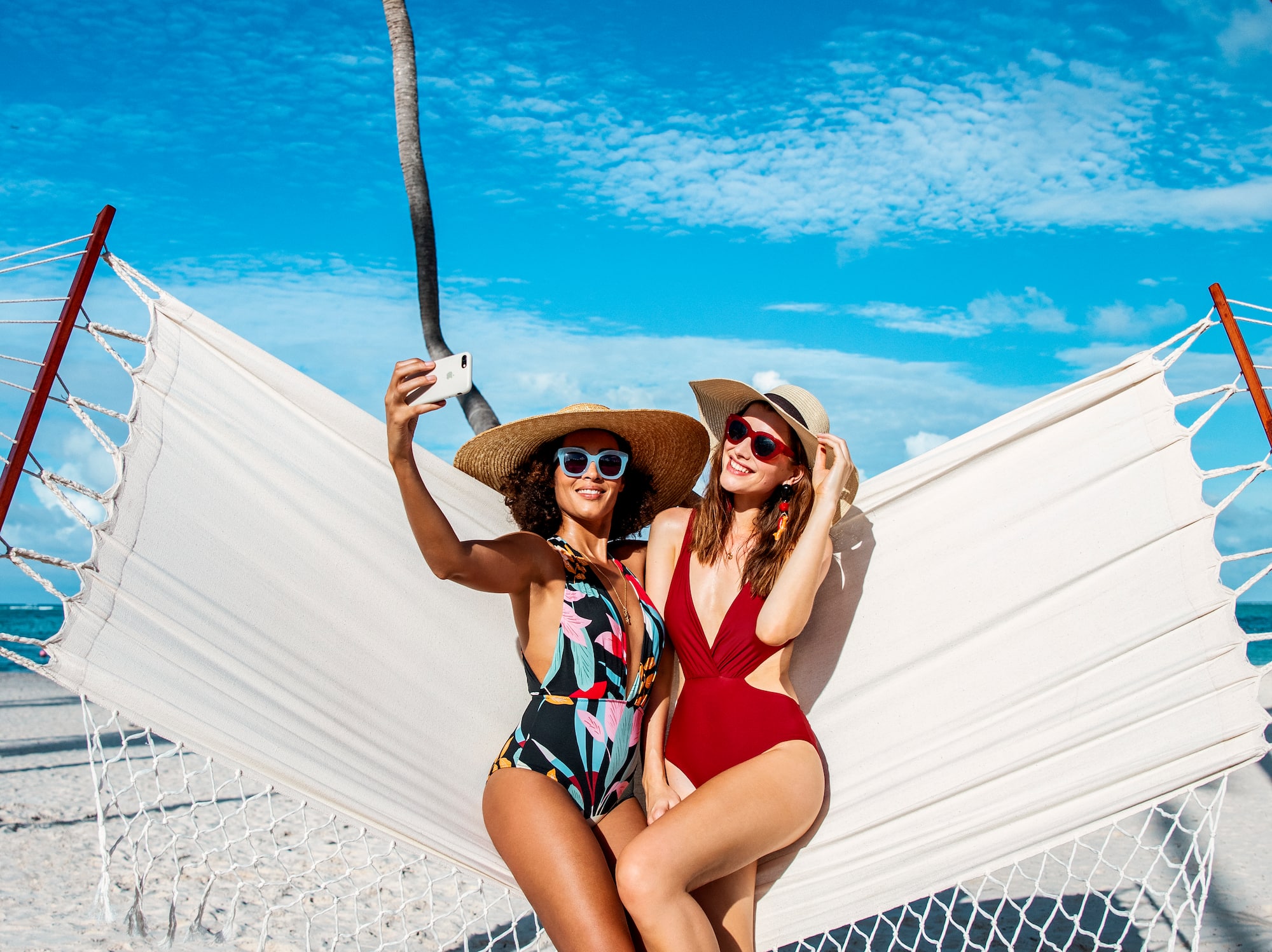 two women in swimsuits and hats sitting in a hammock on a beach