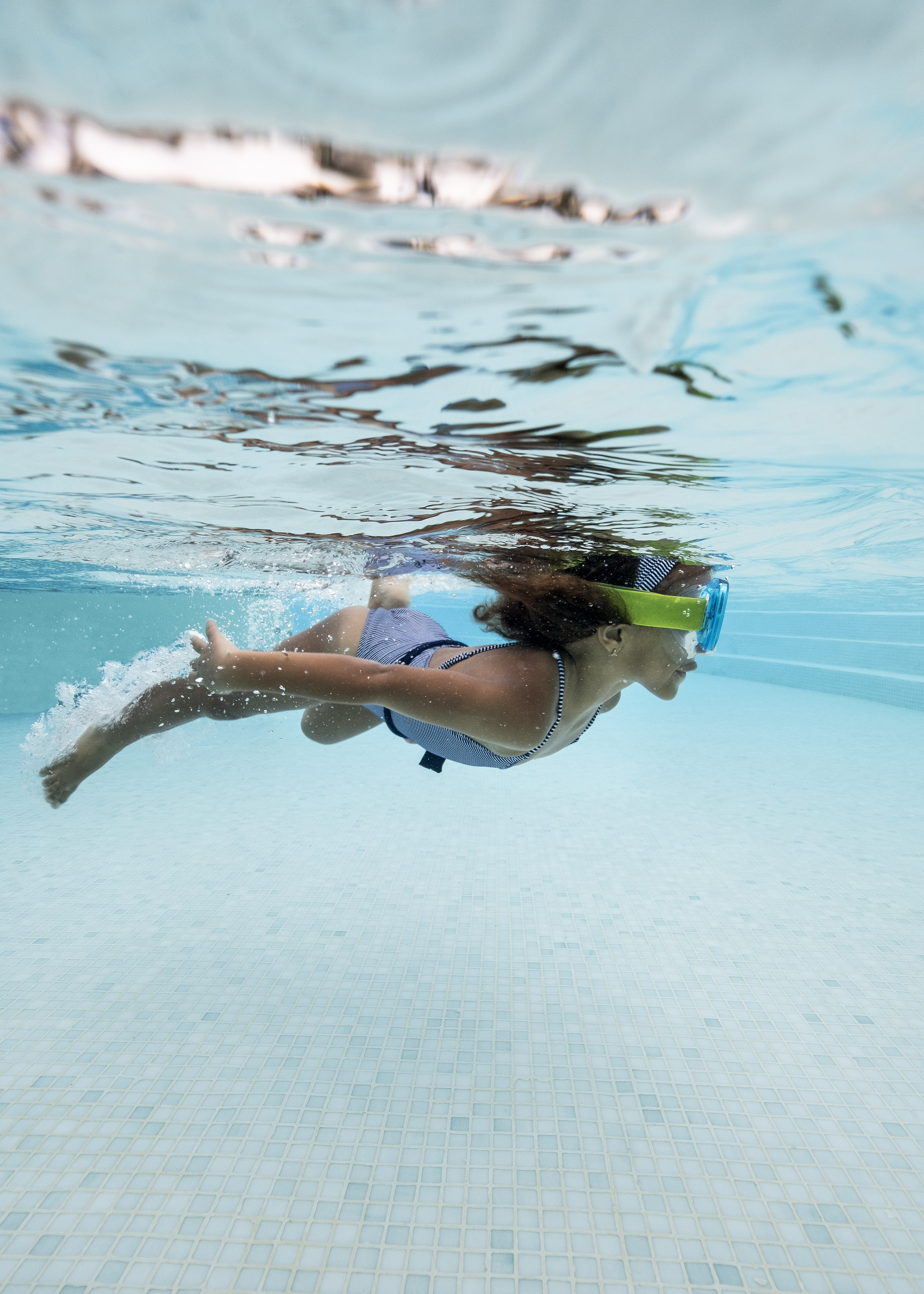 Girl in green goggles swimming underwater in a swimming pool.