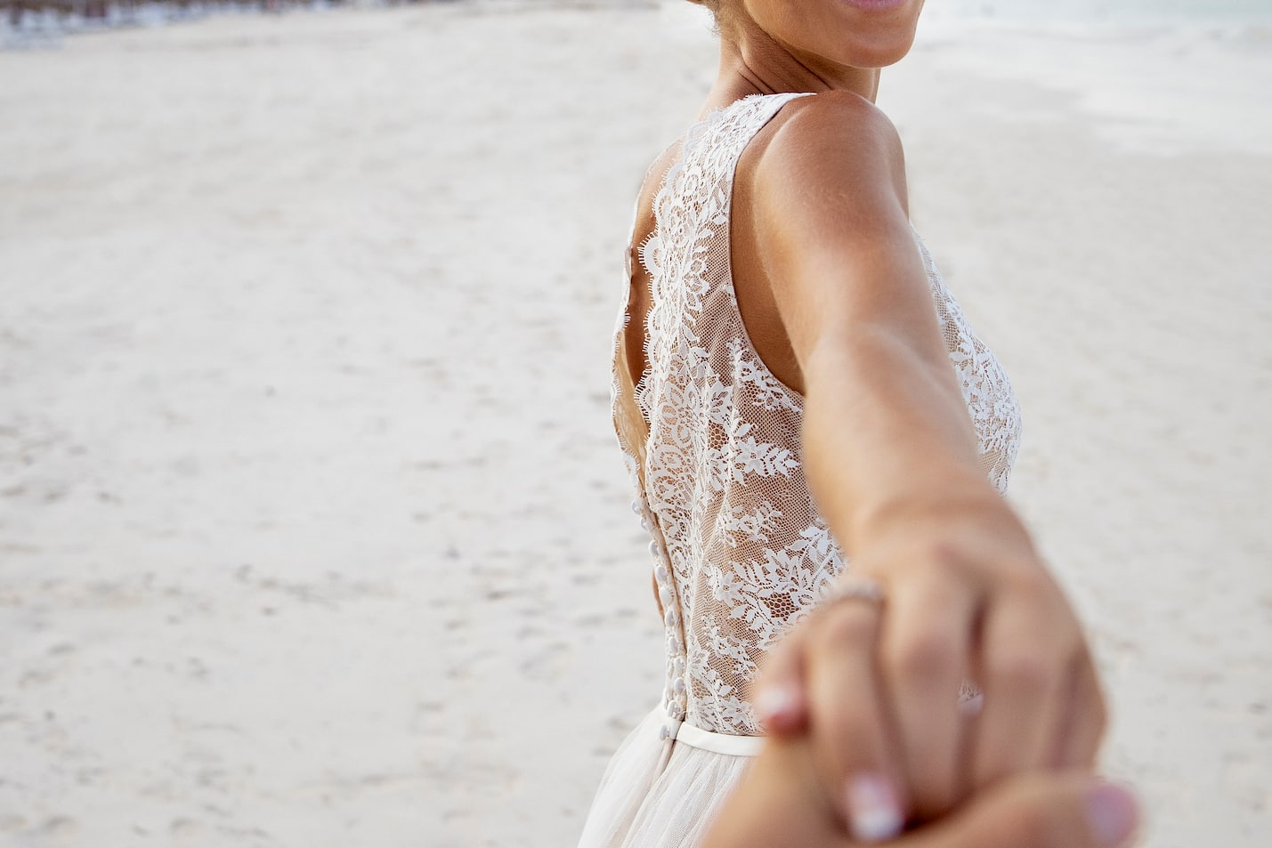 a woman in a white dress holding a hand of a man on a beach
