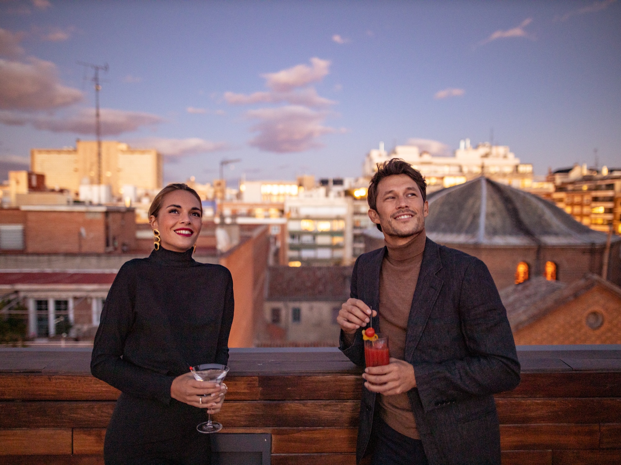 A man and a woman are enjoying drinks on a balcony.