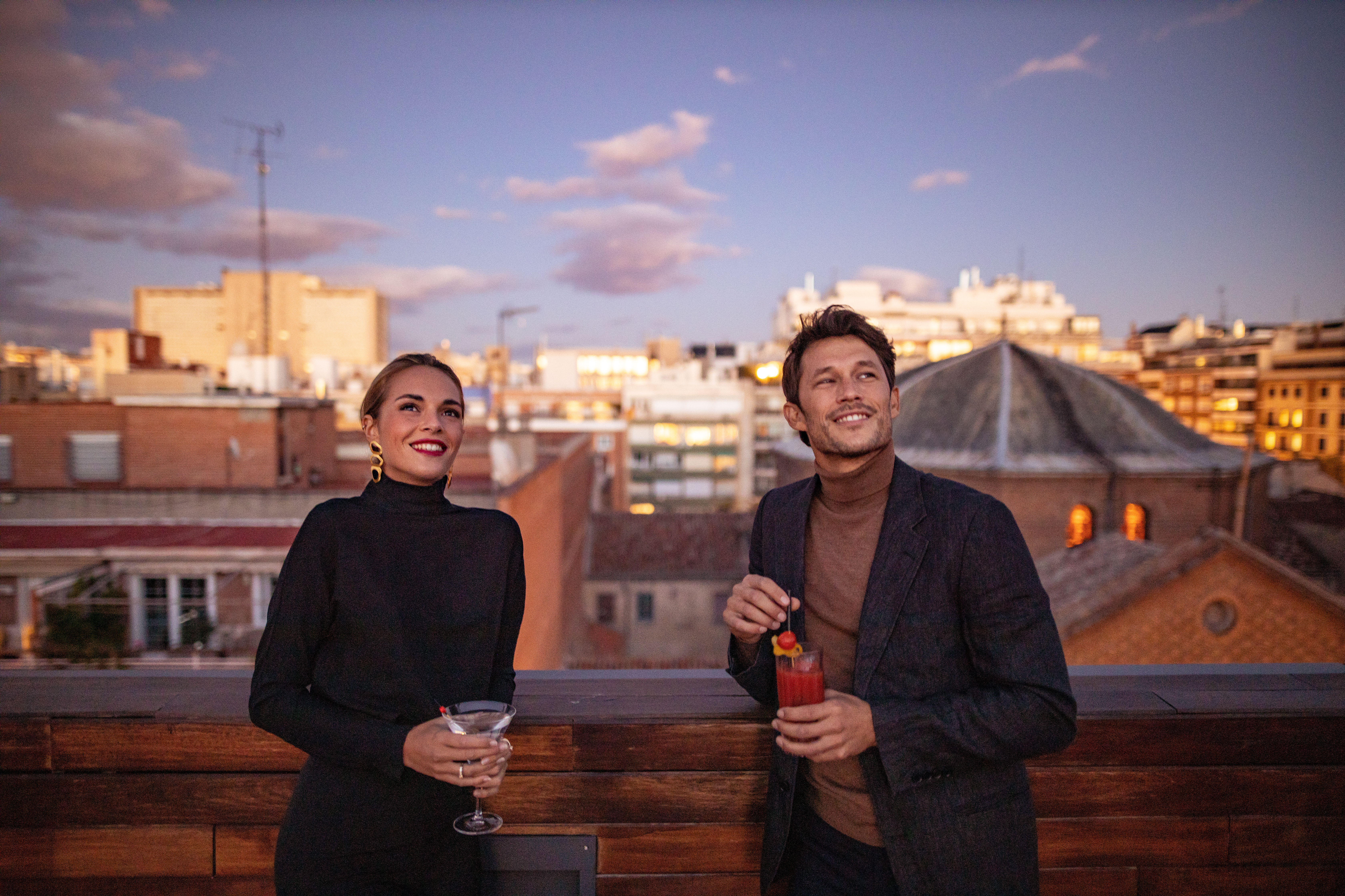 A man and a woman are enjoying drinks on a balcony.