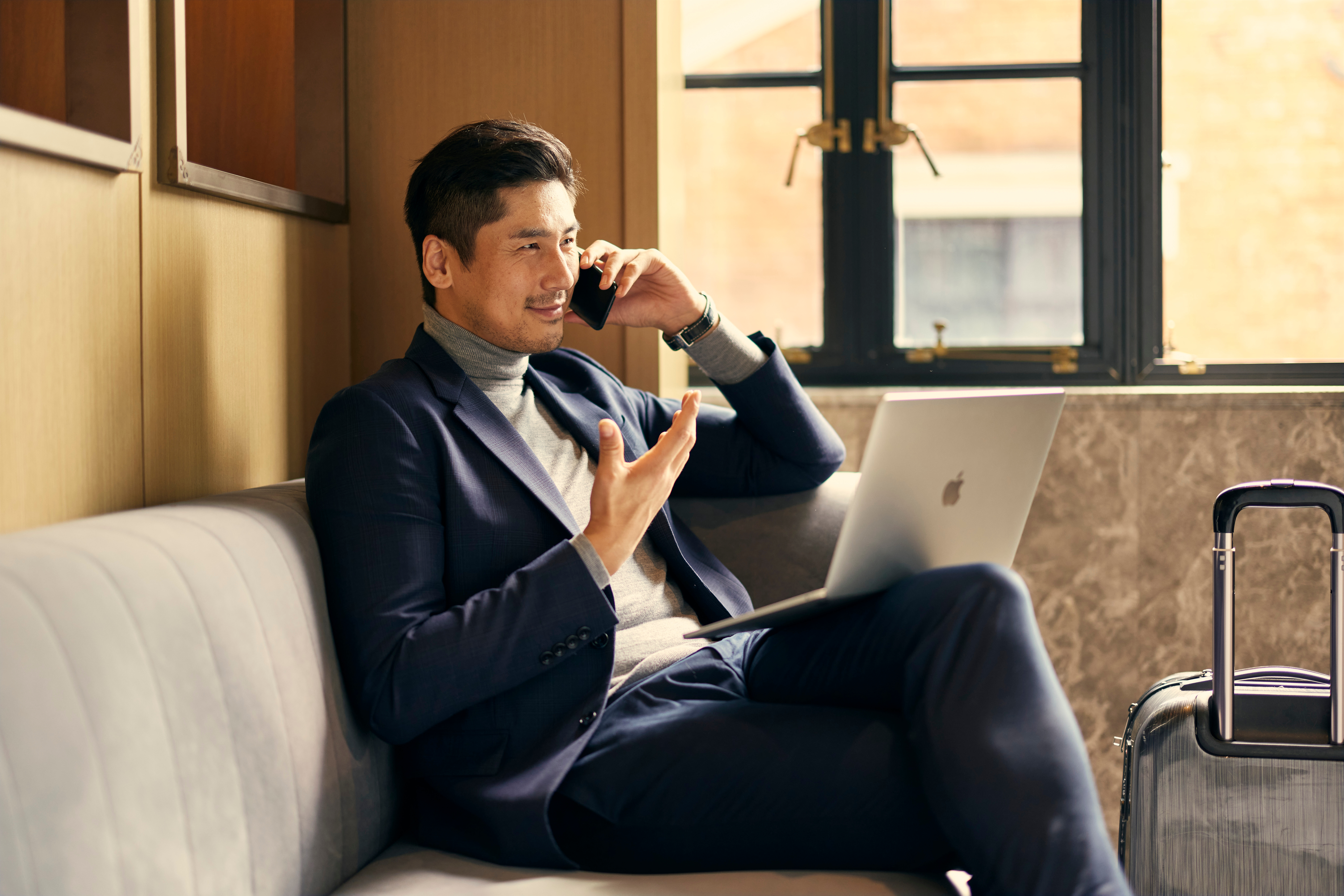 a man sitting on a couch talking on a phone and using a laptop
