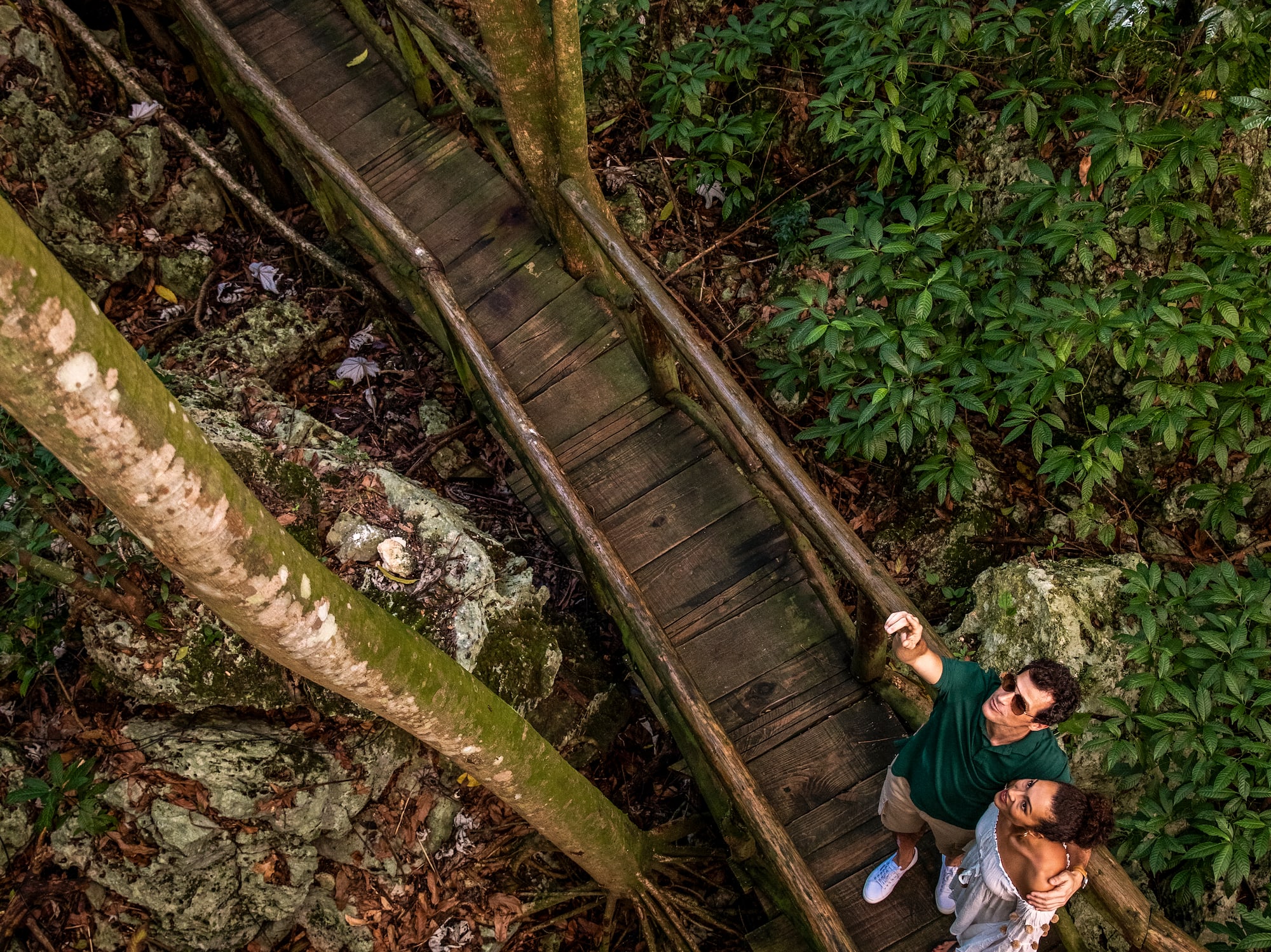 a man and woman standing on a wooden bridge in the woods