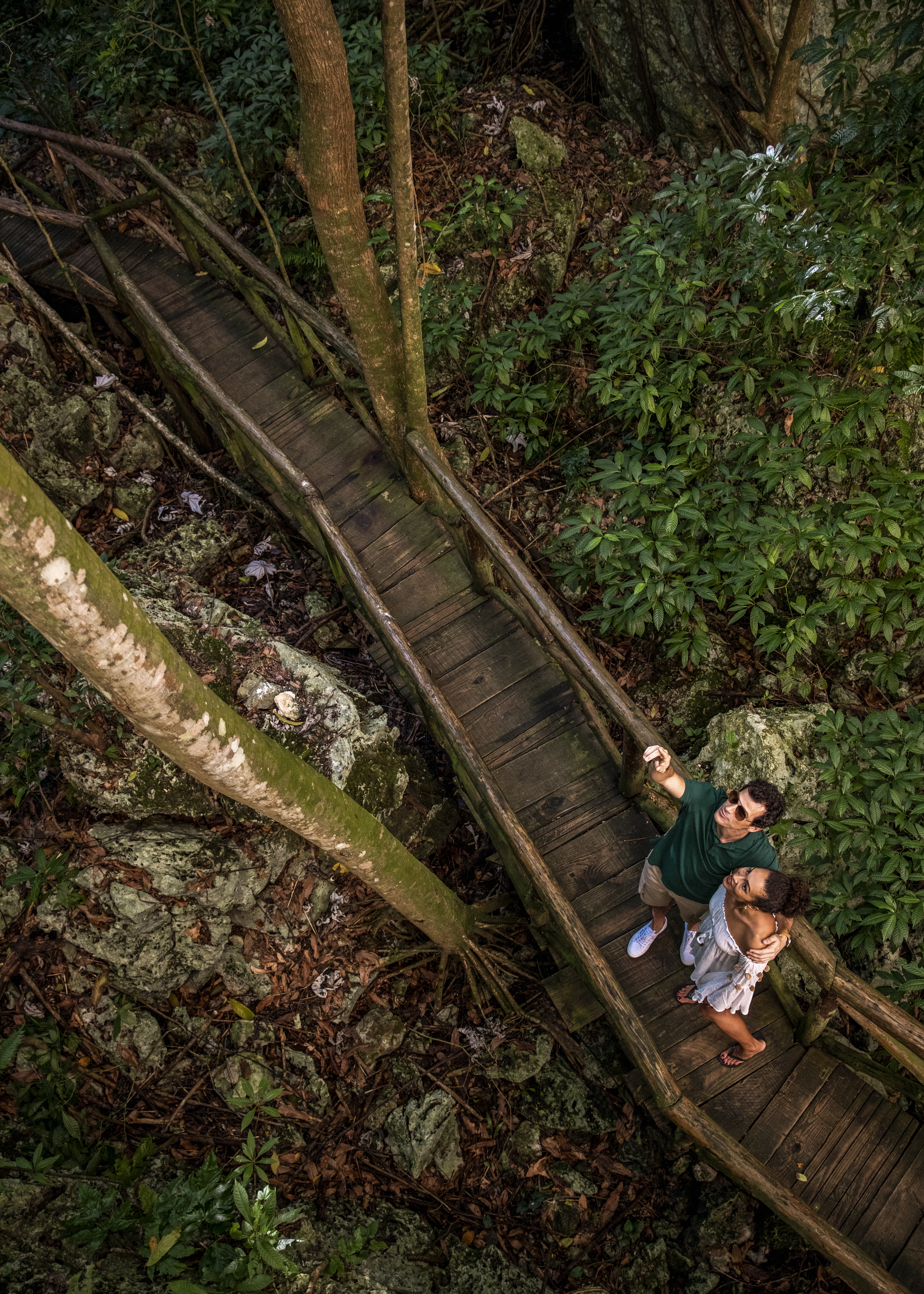 a man and woman standing on a wooden bridge in the woods