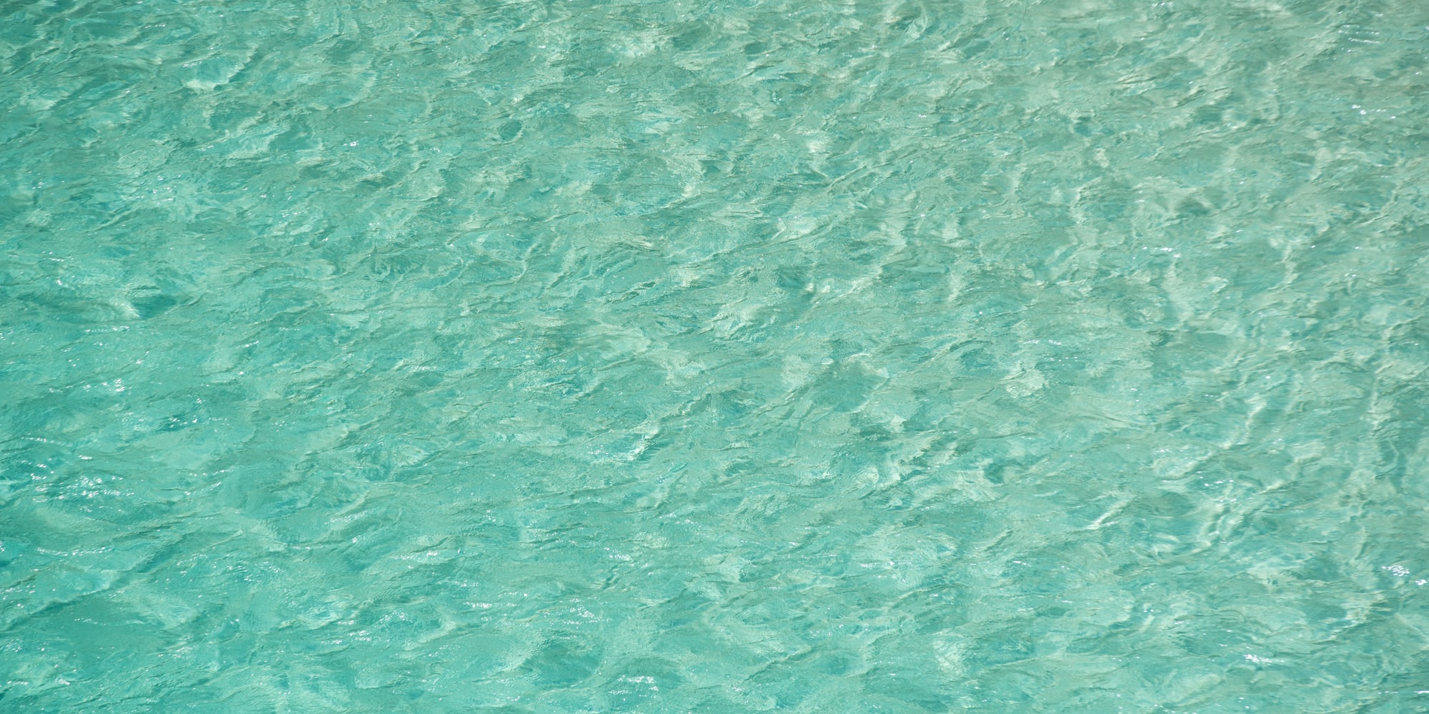Agua turquesa cristalina con ondas y reflejos de sol.