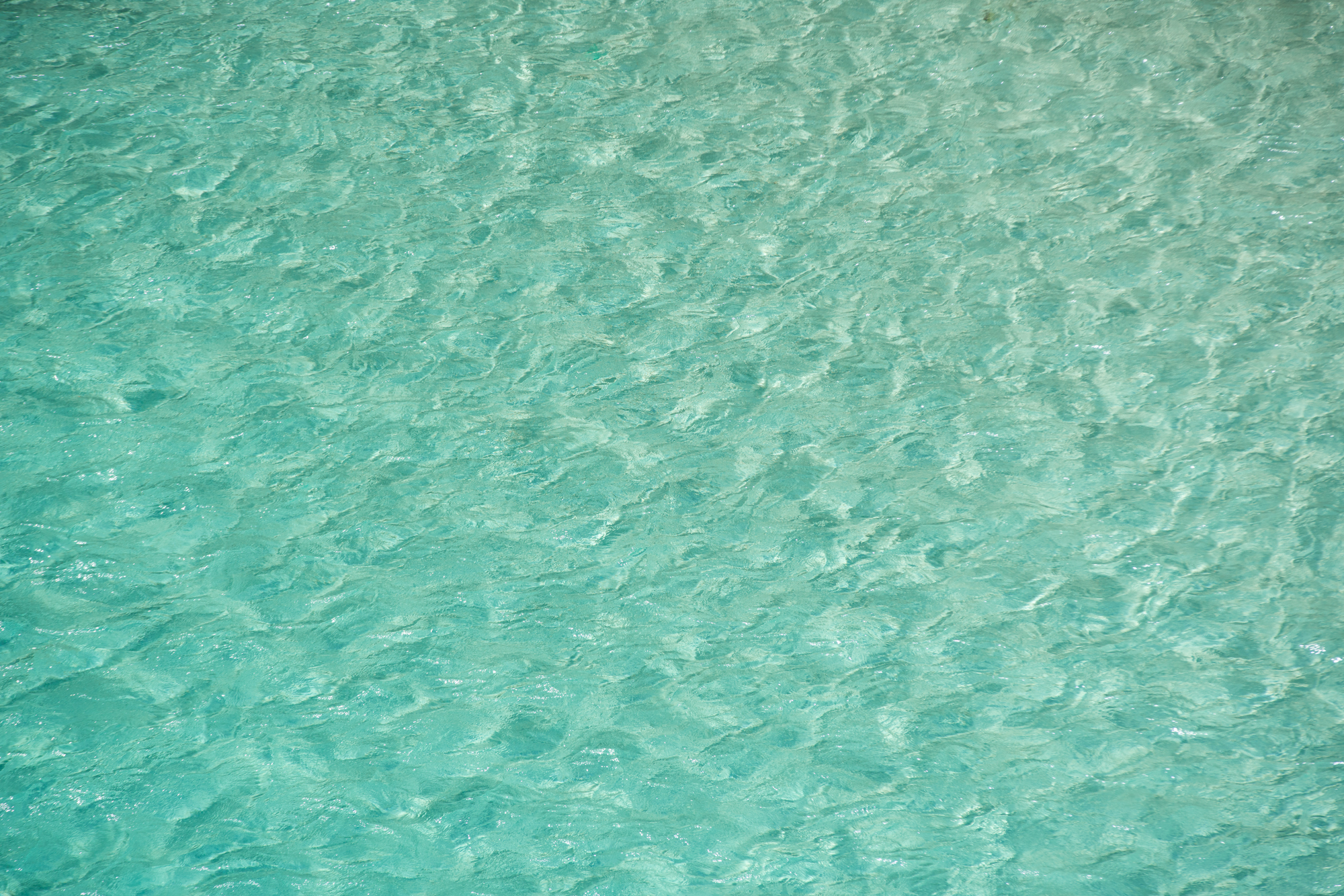 Agua turquesa cristalina con ondas y reflejos de sol.