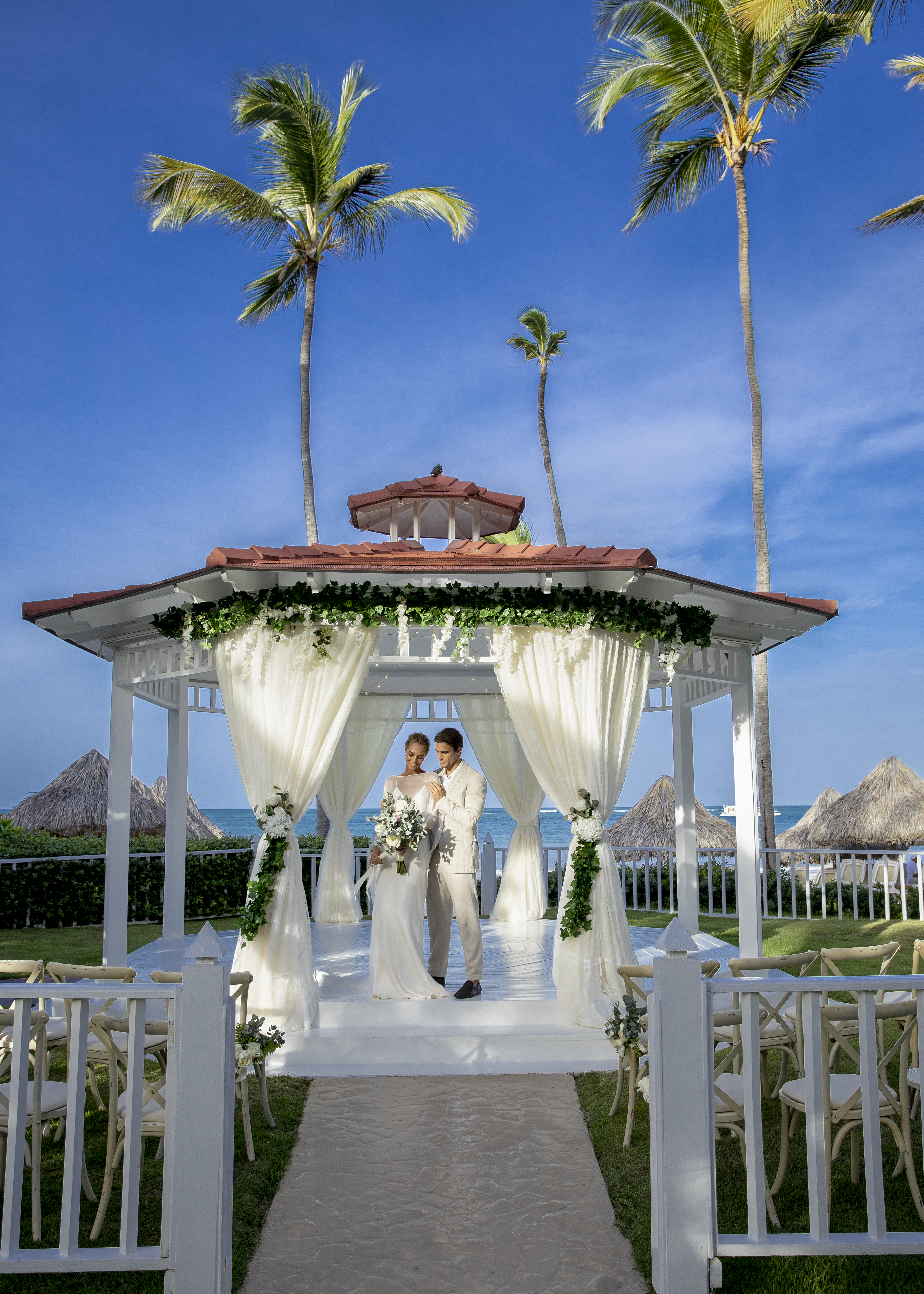 Bride and groom at a tropical beach wedding in a white gazebo, ocean background.