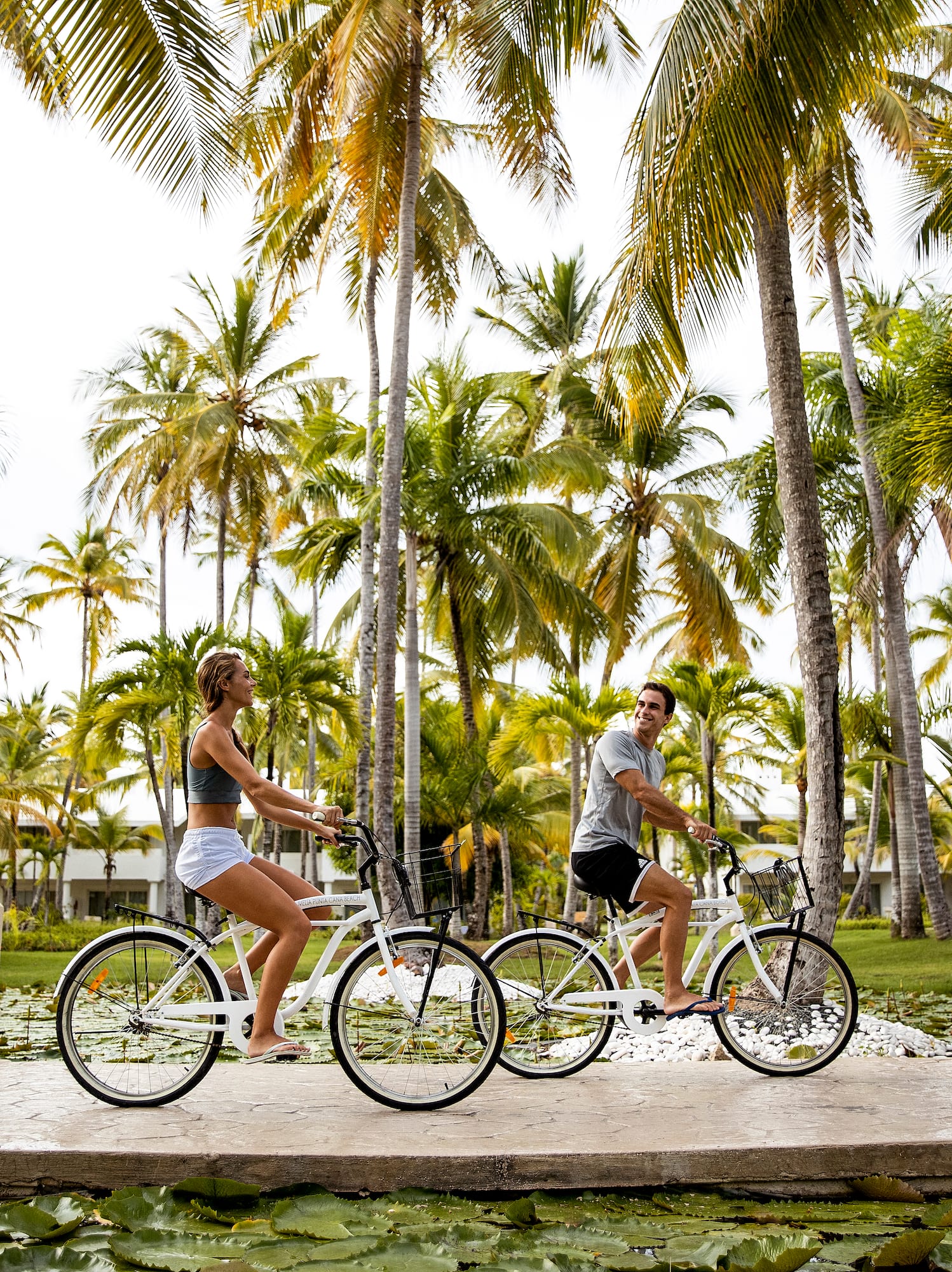 a man and woman riding bicycles under palm trees