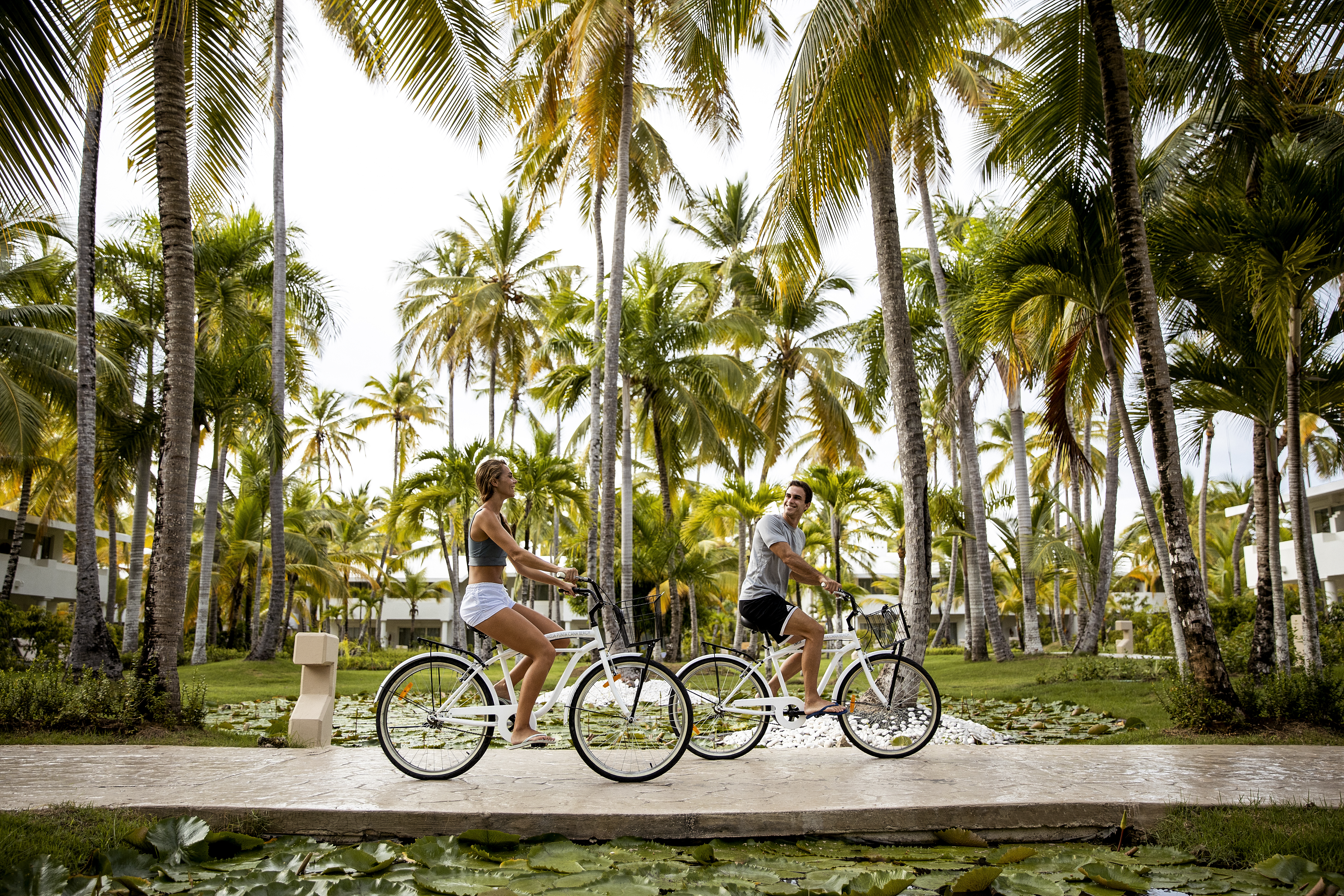 Happy couple cycling on resort path lined with tall palm trees.