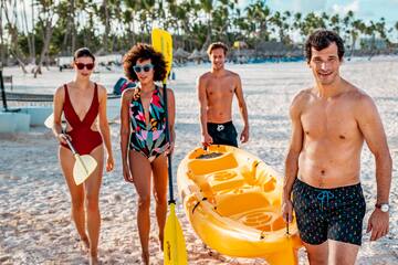 a group of people walking on a beach with a yellow canoe