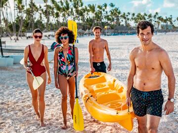a group of people walking on a beach with a yellow canoe