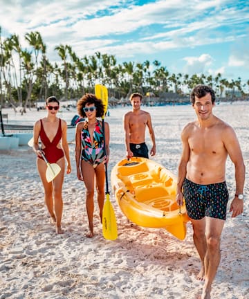 a group of people walking on a beach with a yellow canoe