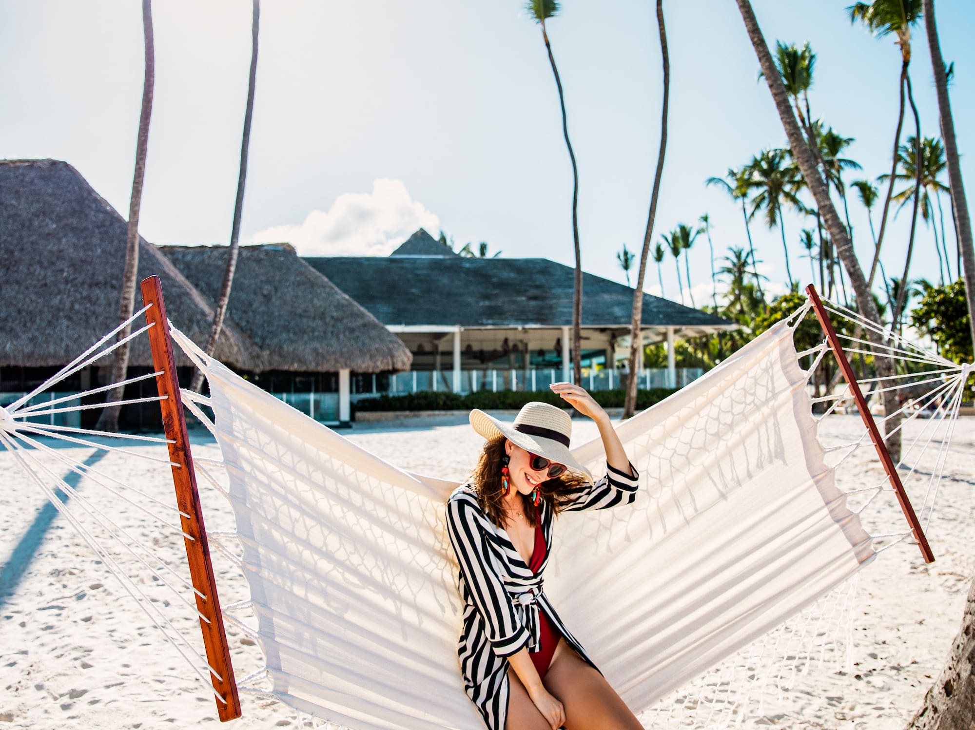 a woman in a swimsuit and hat sitting in a hammock on a beach