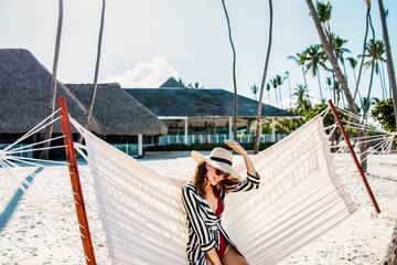 a woman in a swimsuit and hat sitting in a hammock on a beach