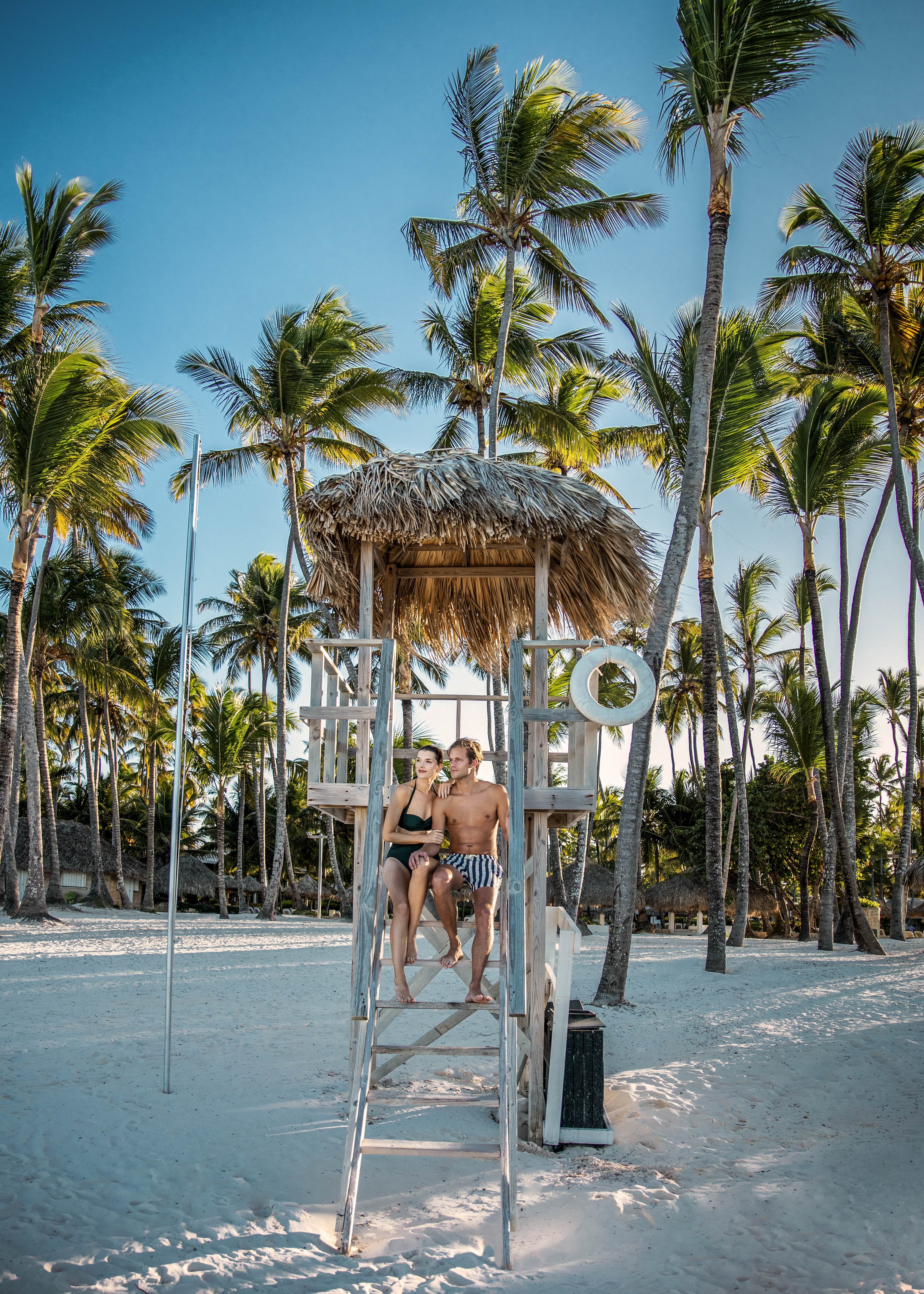 a man and woman sitting on a lifeguard tower on a beach