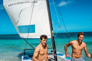 two men in swim trunks on a sailboat