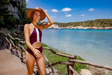 a woman in a swimsuit and hat standing on a path by water