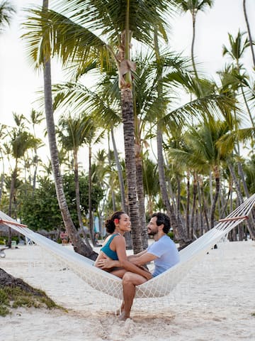 a man and woman sitting in a hammock on a beach