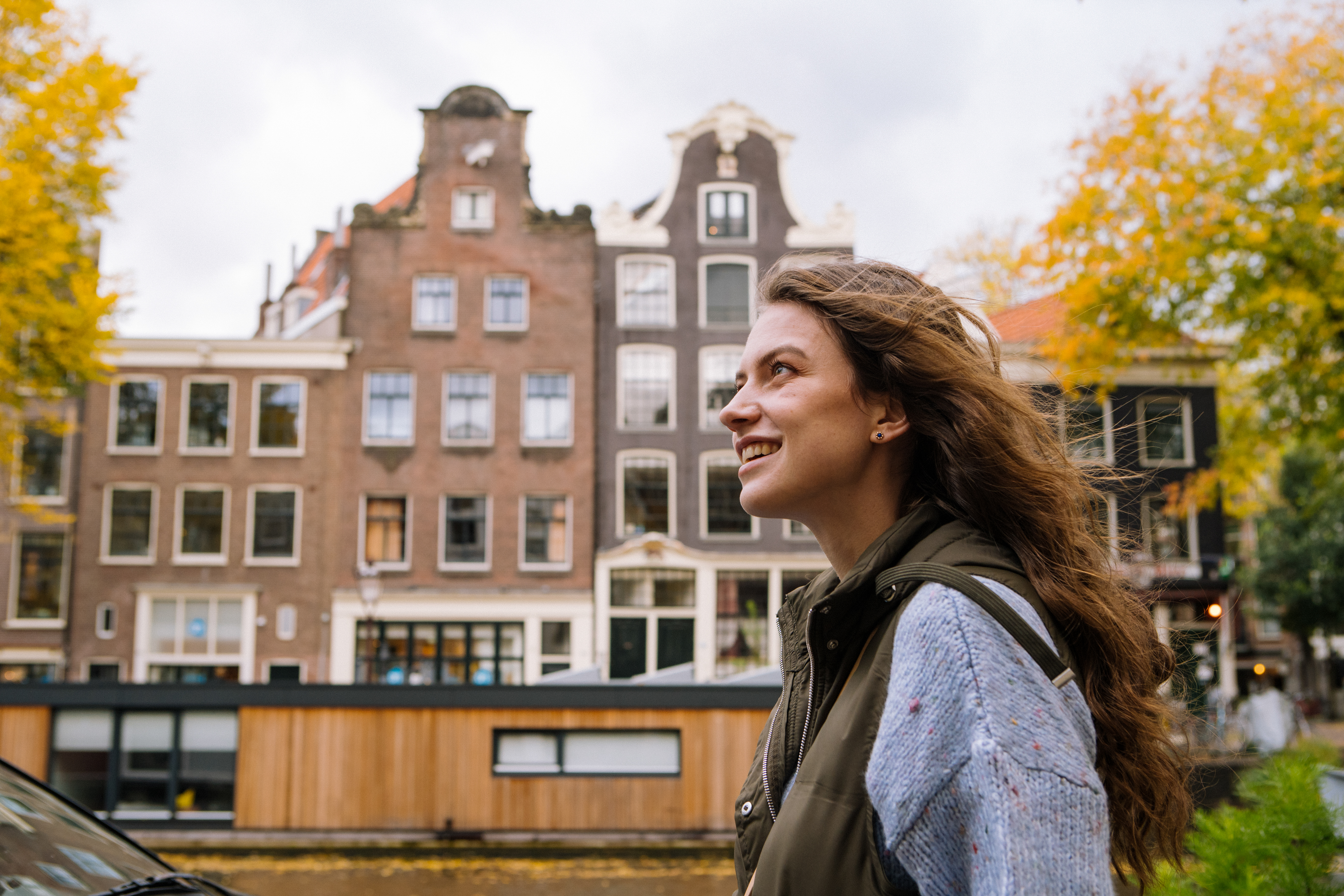 Smiling woman, Amsterdam canal houses, autumn yellow foliage.