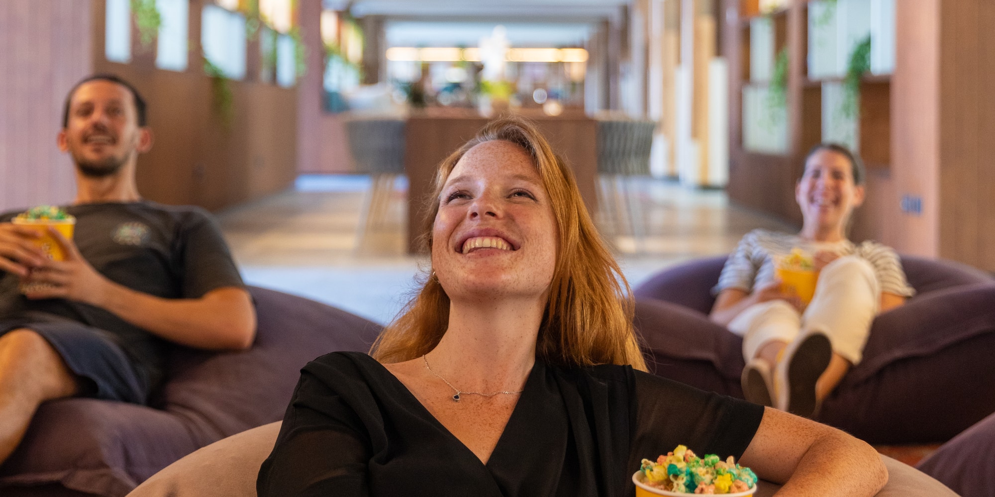 a woman sitting on bean bags with a bucket of popcorn and a man in the background