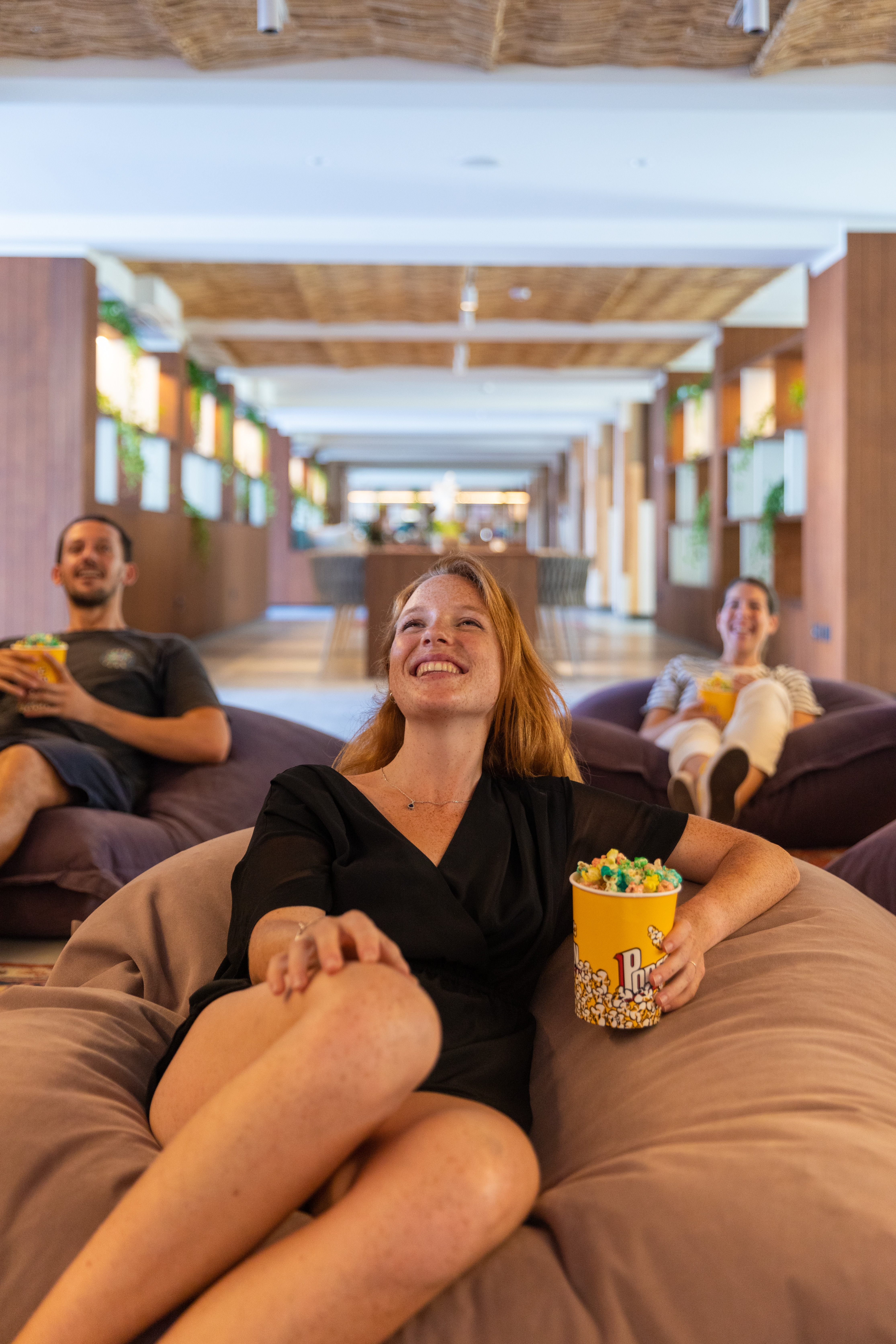 a woman sitting on bean bags with a bucket of popcorn and a man in the background