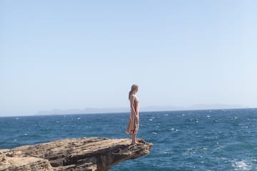 a woman standing on a cliff edge overlooking the ocean
