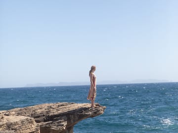 a woman standing on a cliff edge overlooking the ocean