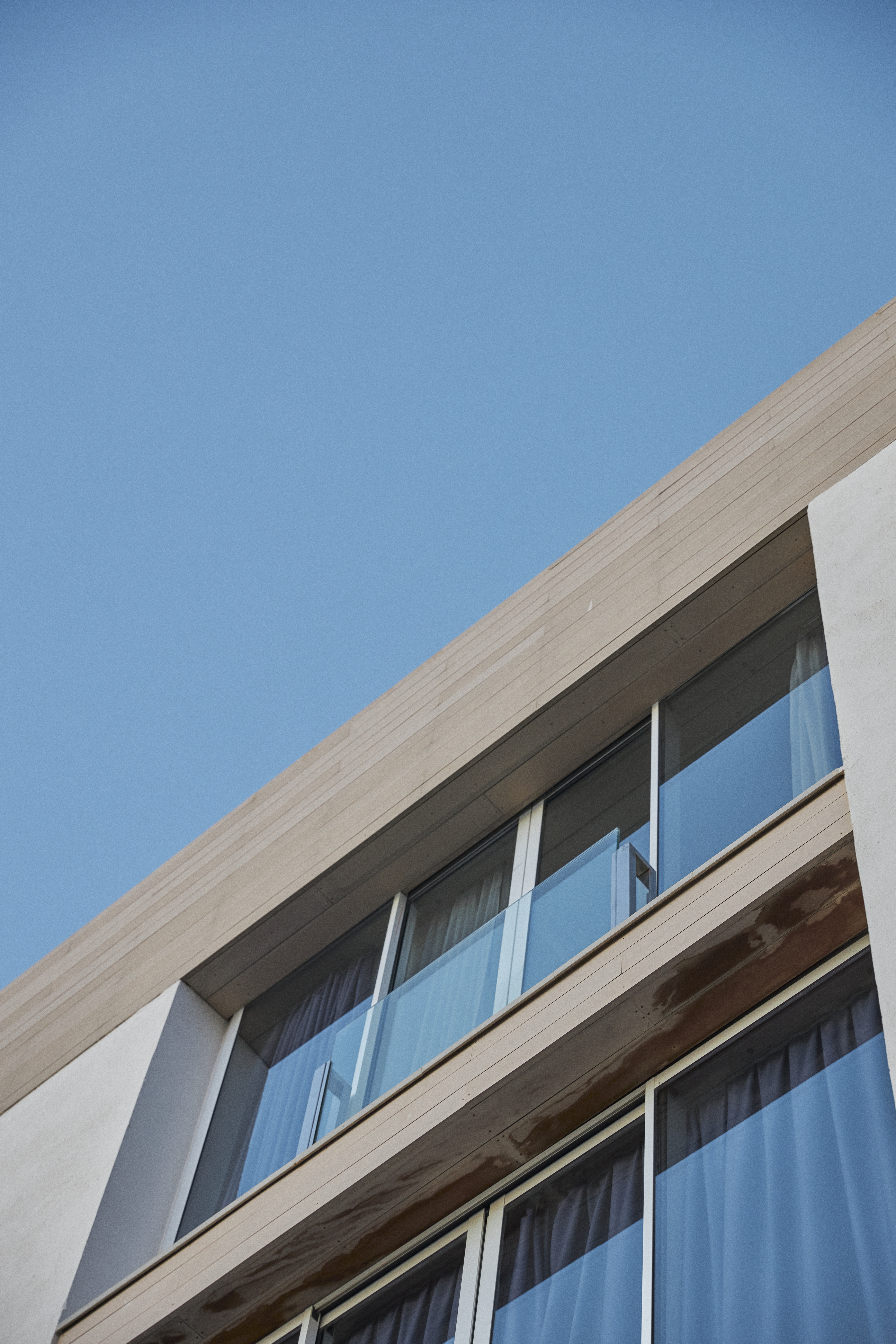 Modern building facade with large windows, glass balconies, and blue sky.