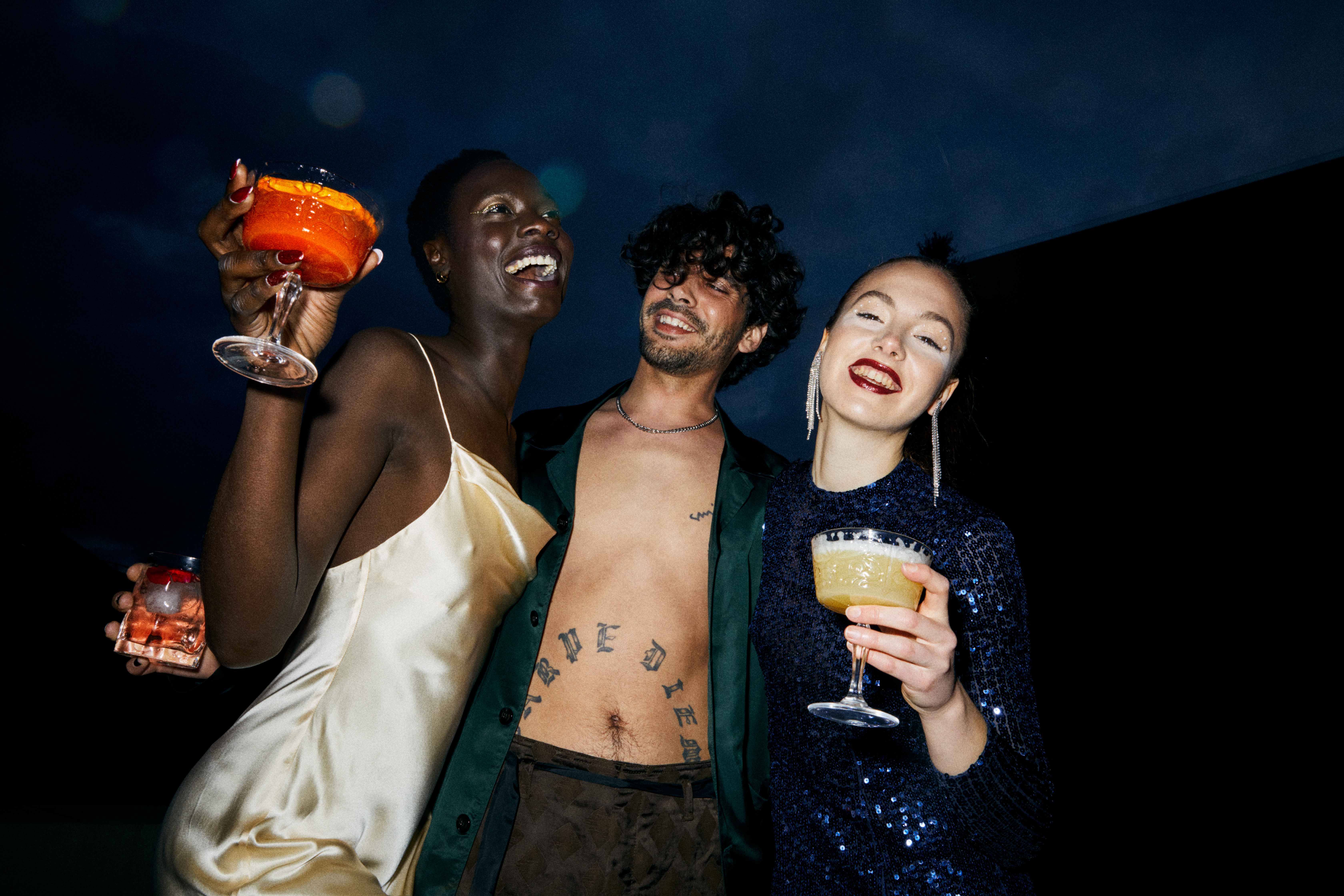 Diverse friends enjoying cocktails and laughing at a festive night party.
