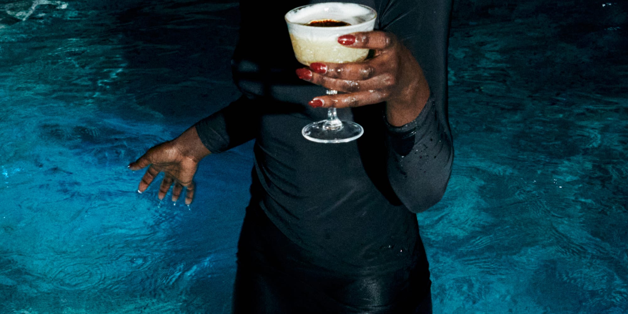 a woman in a black dress holding a drink in a pool