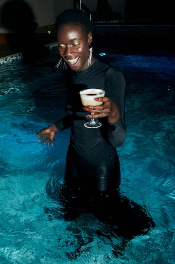 a woman in a black dress holding a drink in a pool