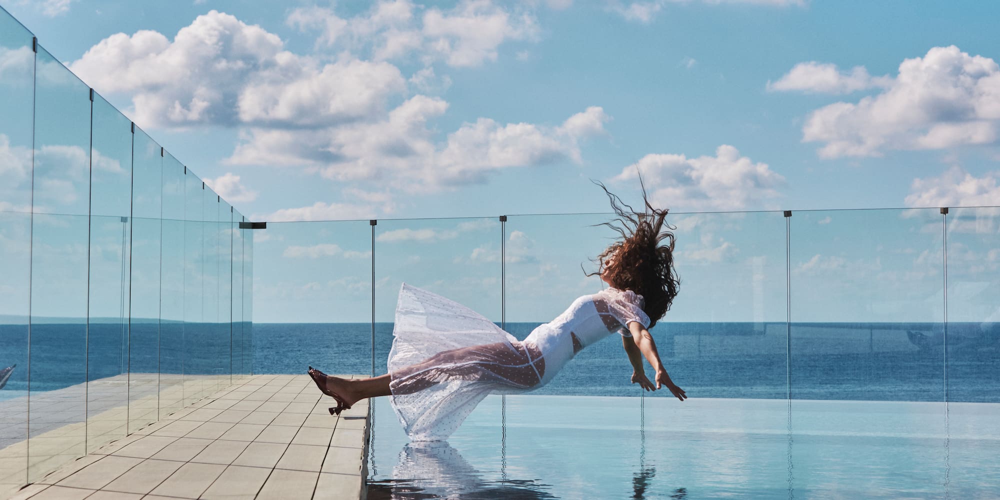 a woman in a white dress jumping into a pool of water