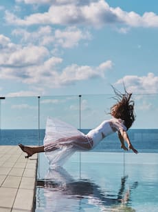 a woman in a white dress jumping into a pool of water
