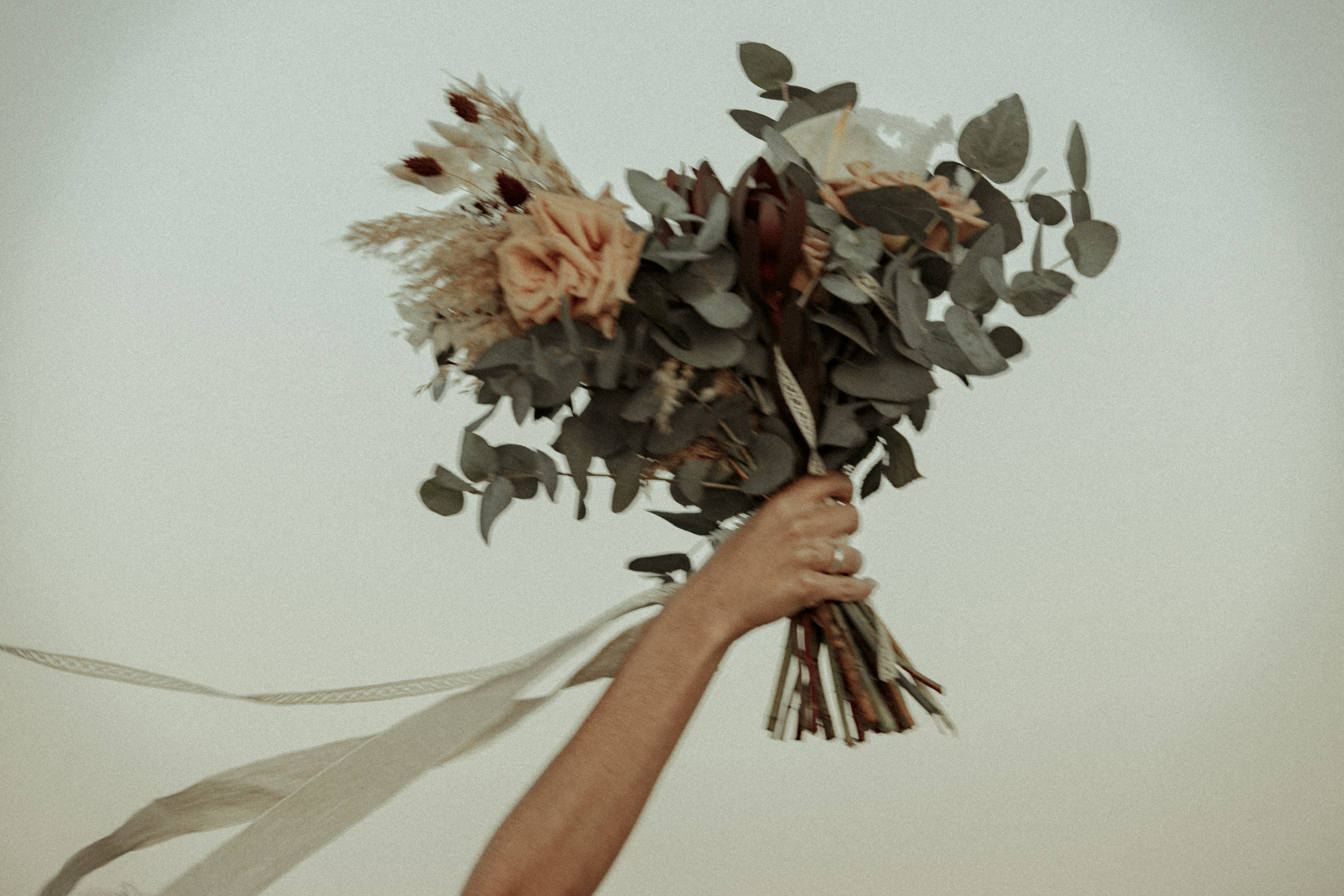Bridal bouquet with peach roses, eucalyptus, dried accents, and flowing ribbons.