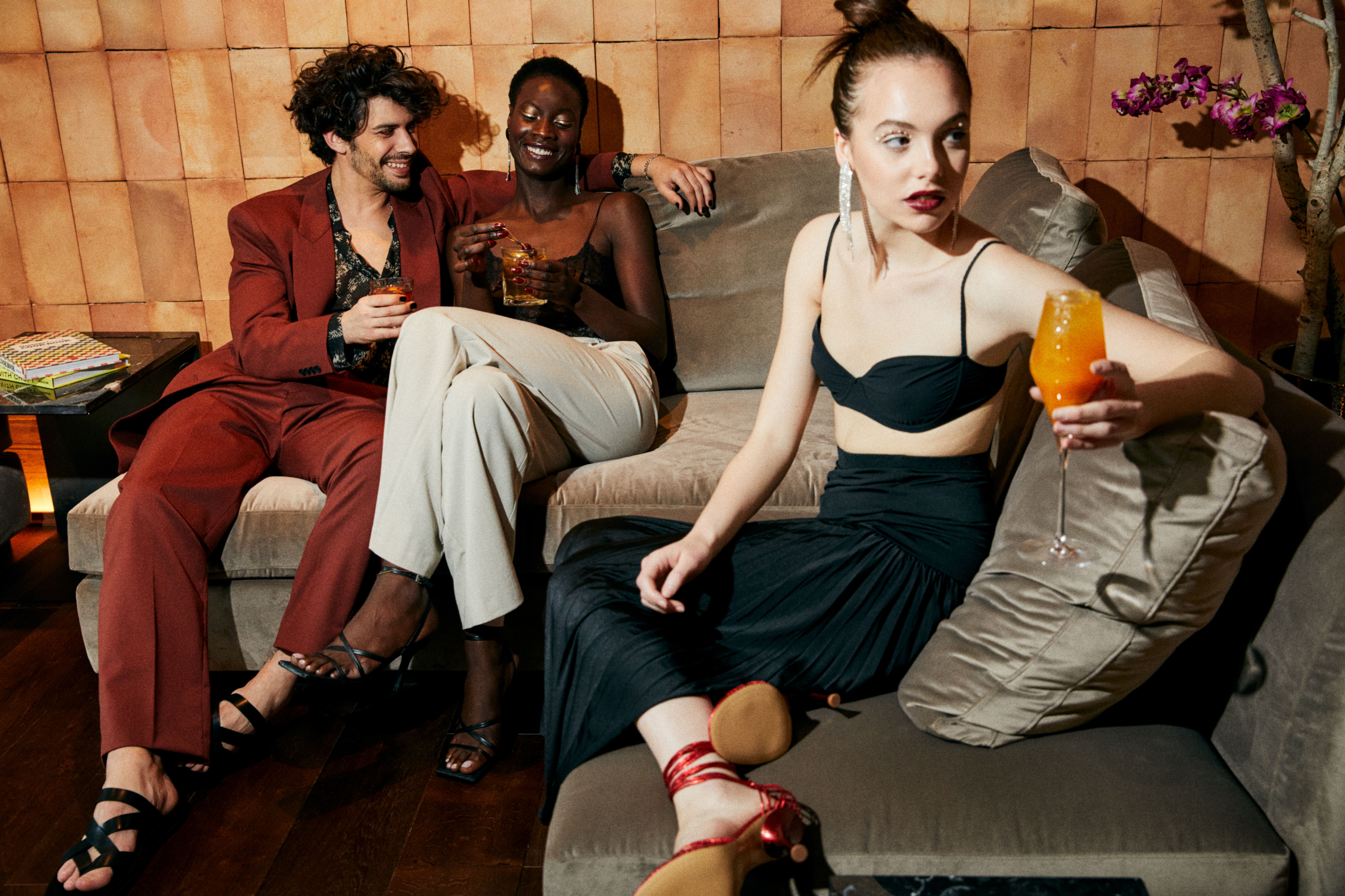 Diverse group of friends in chic outfits enjoying drinks on a lounge sofa.