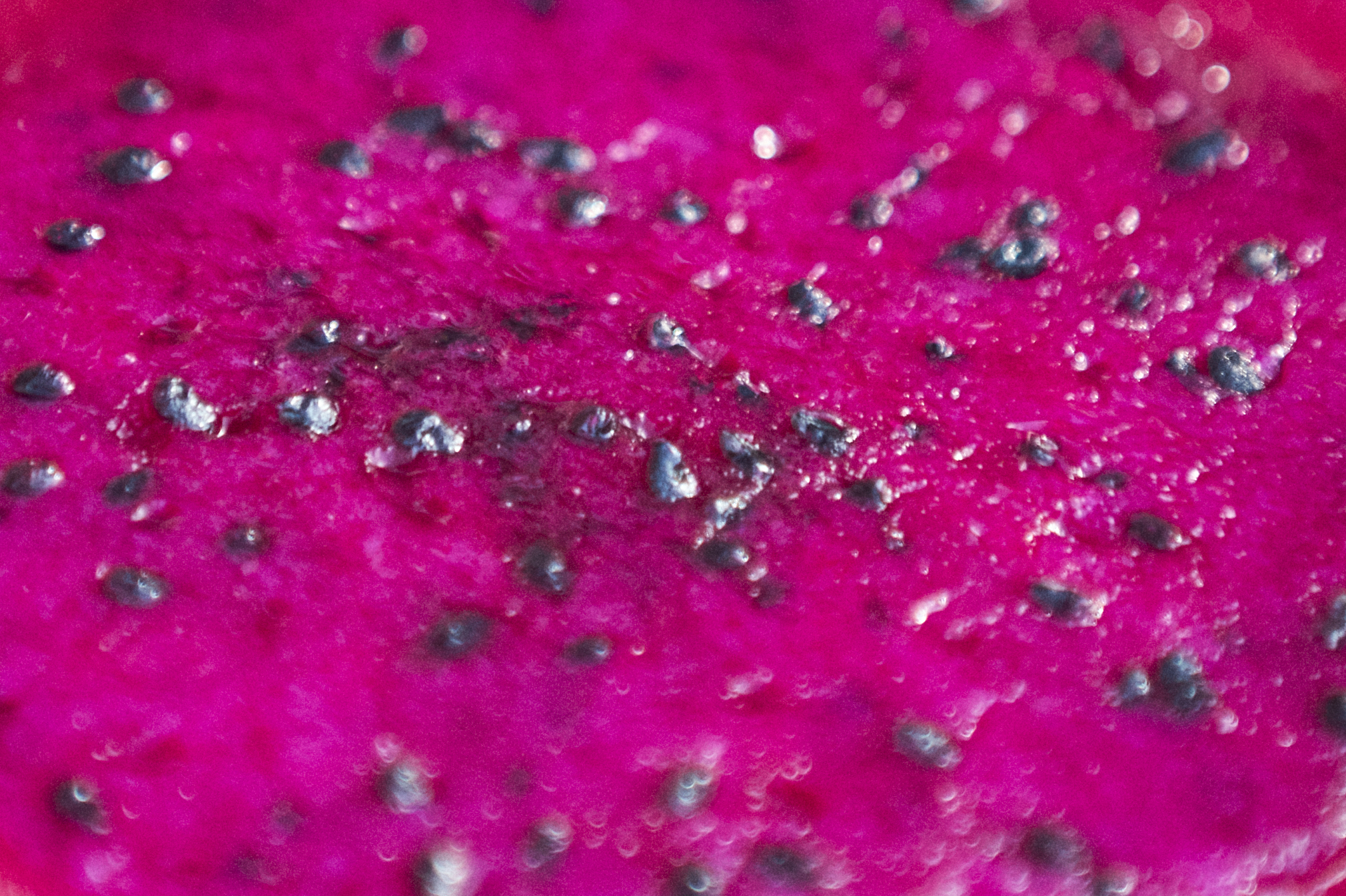 Vibrant pink dragon fruit flesh with dark shiny seeds, close-up.