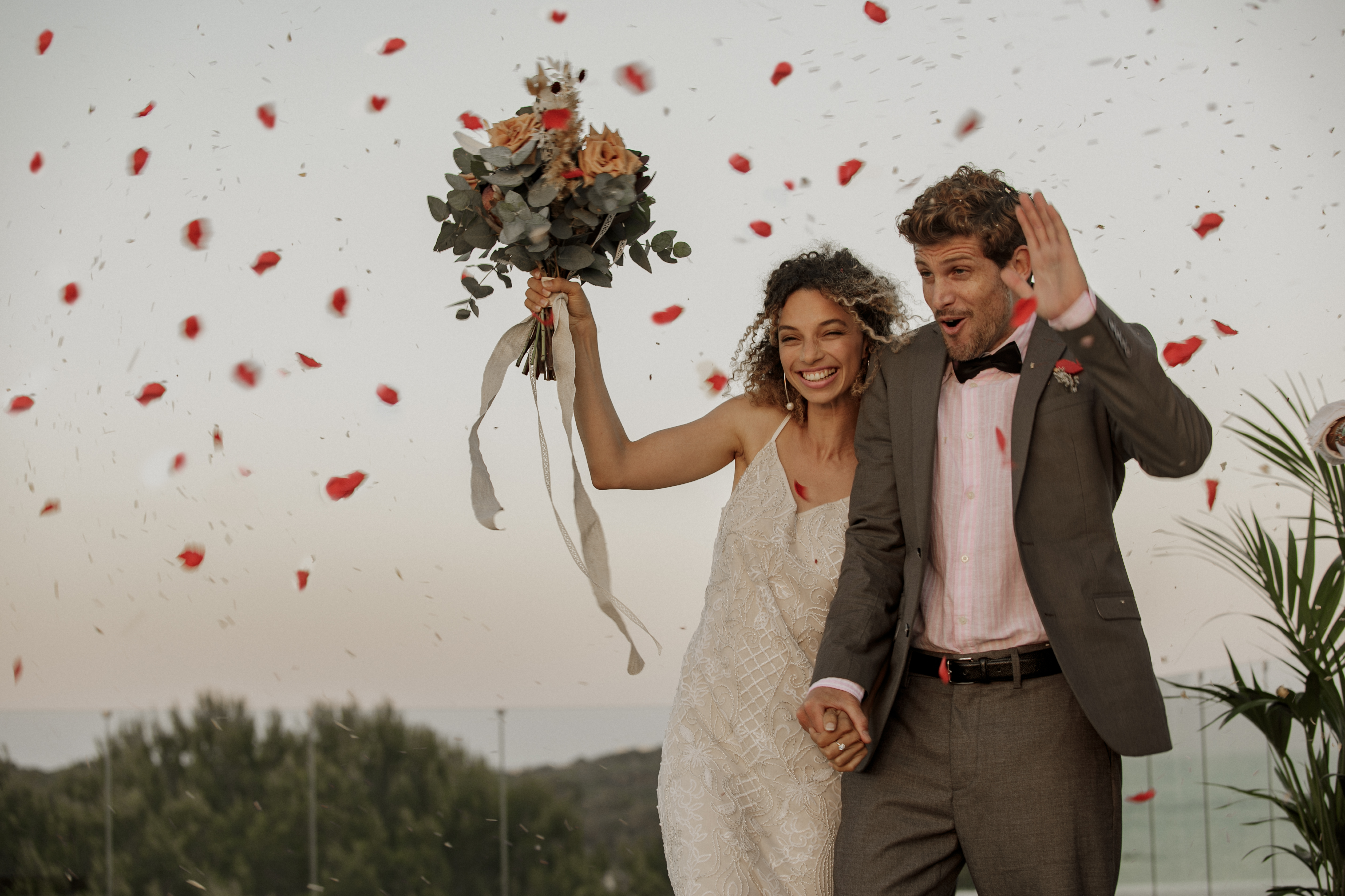 Excited wedding couple holding hands, showered in red rose petals.