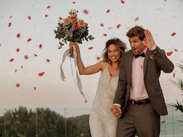 a man and woman holding hands and standing in the air with rose petals falling
