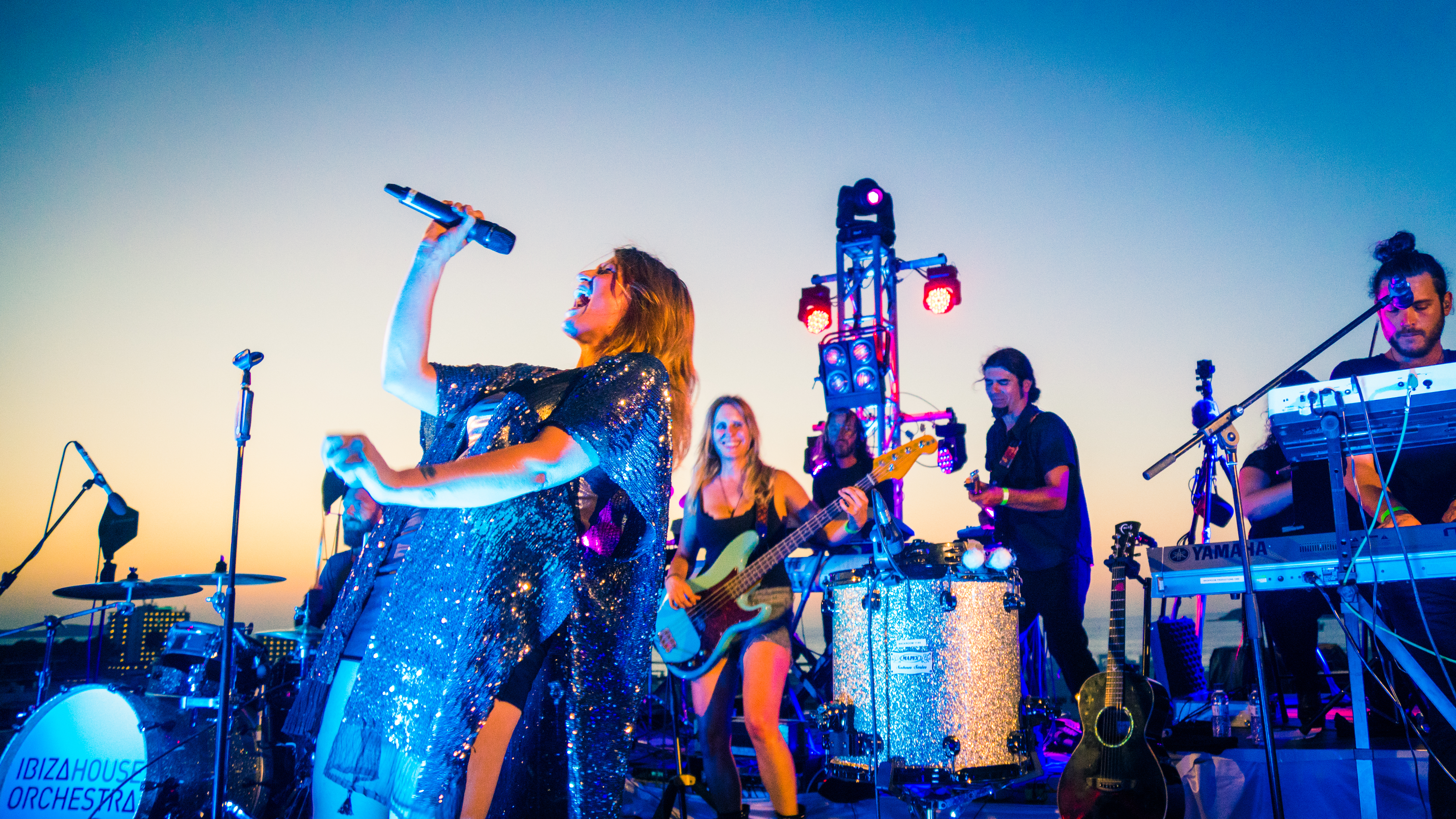 a woman singing into a microphone with people playing instruments