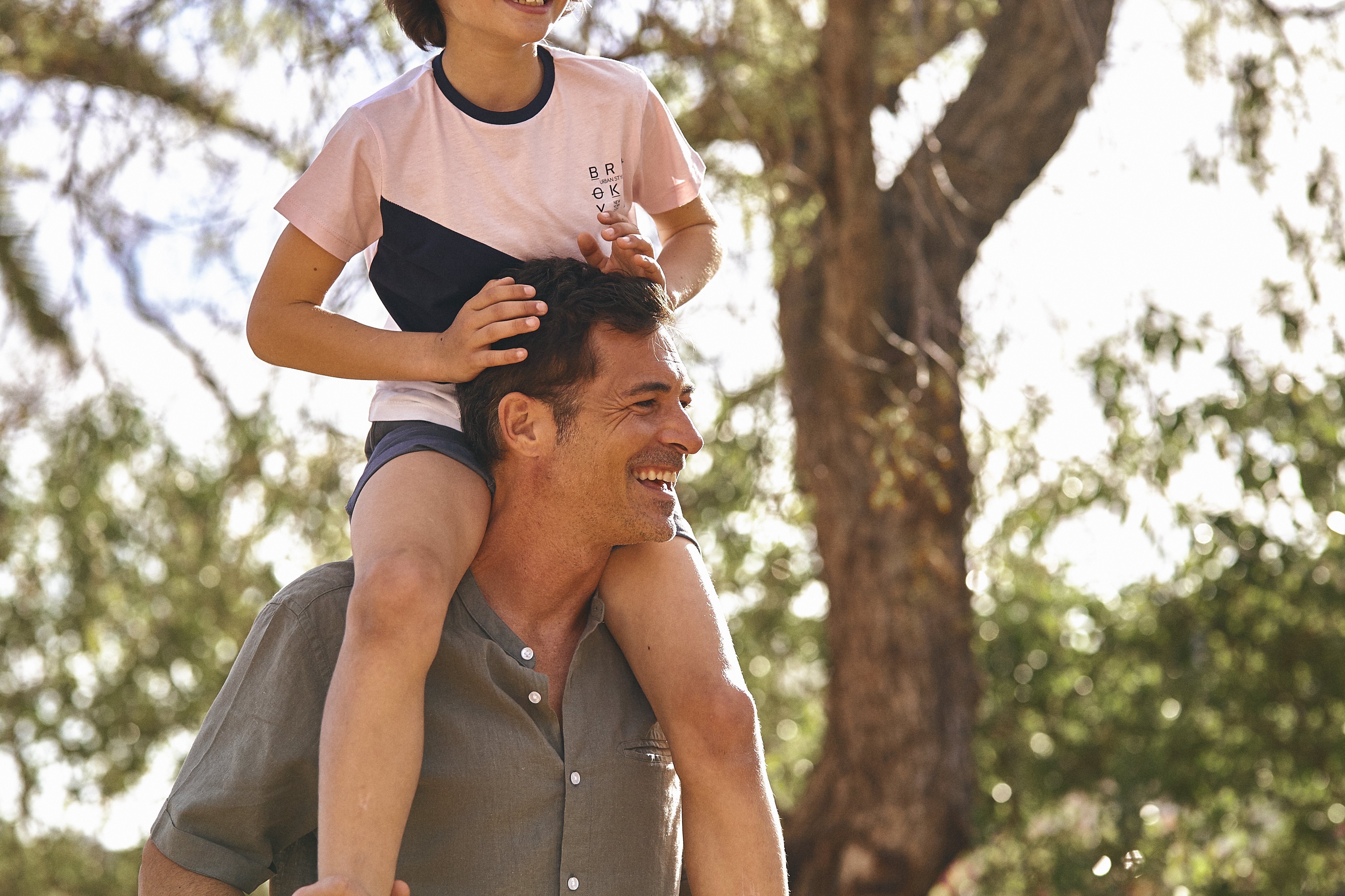 Smiling father carrying son on shoulders outdoors.