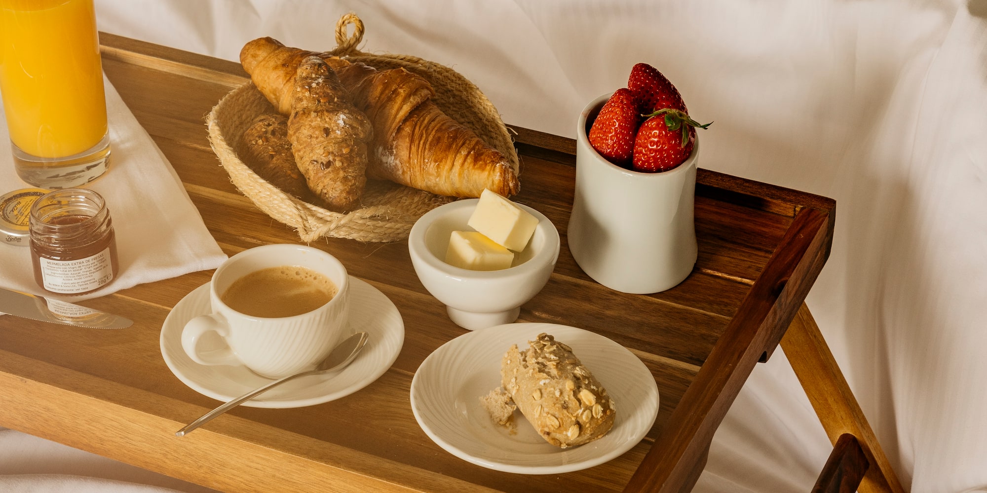 Wooden breakfast tray in bed: croissants, coffee, juice, strawberries.