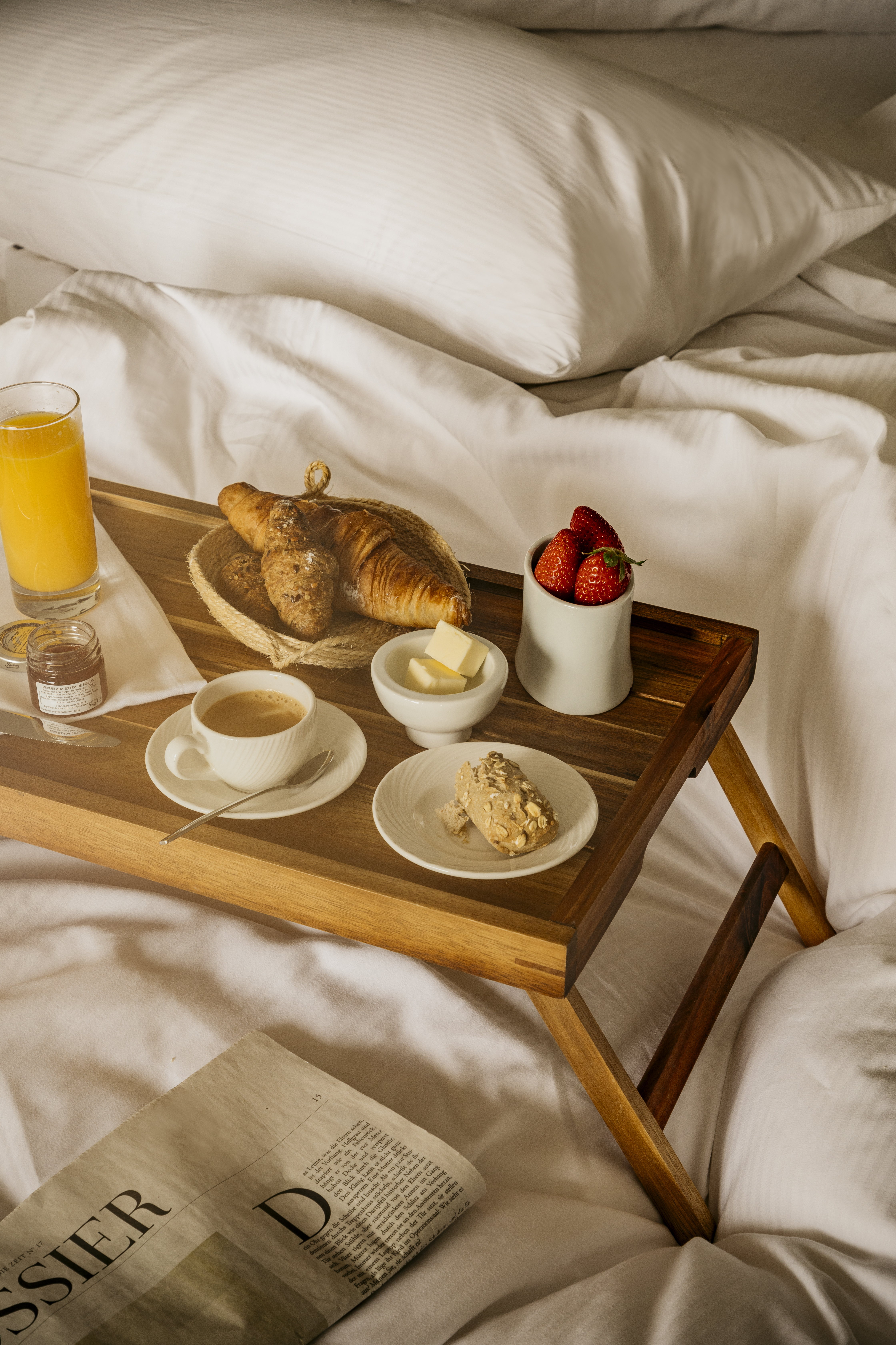 Wooden breakfast tray in bed: croissants, coffee, juice, strawberries.
