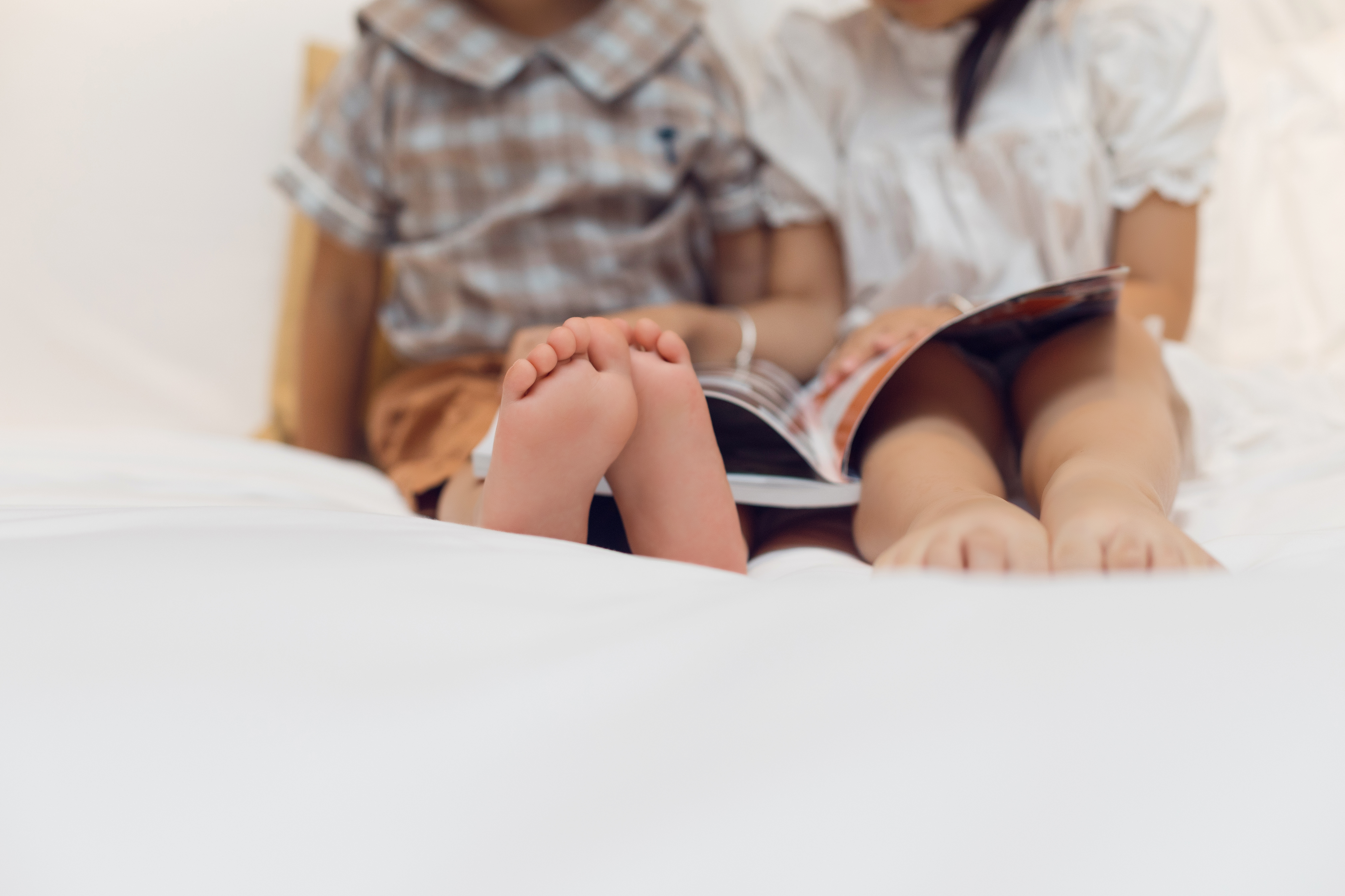 Two children sit on a bed, absorbed in a book.