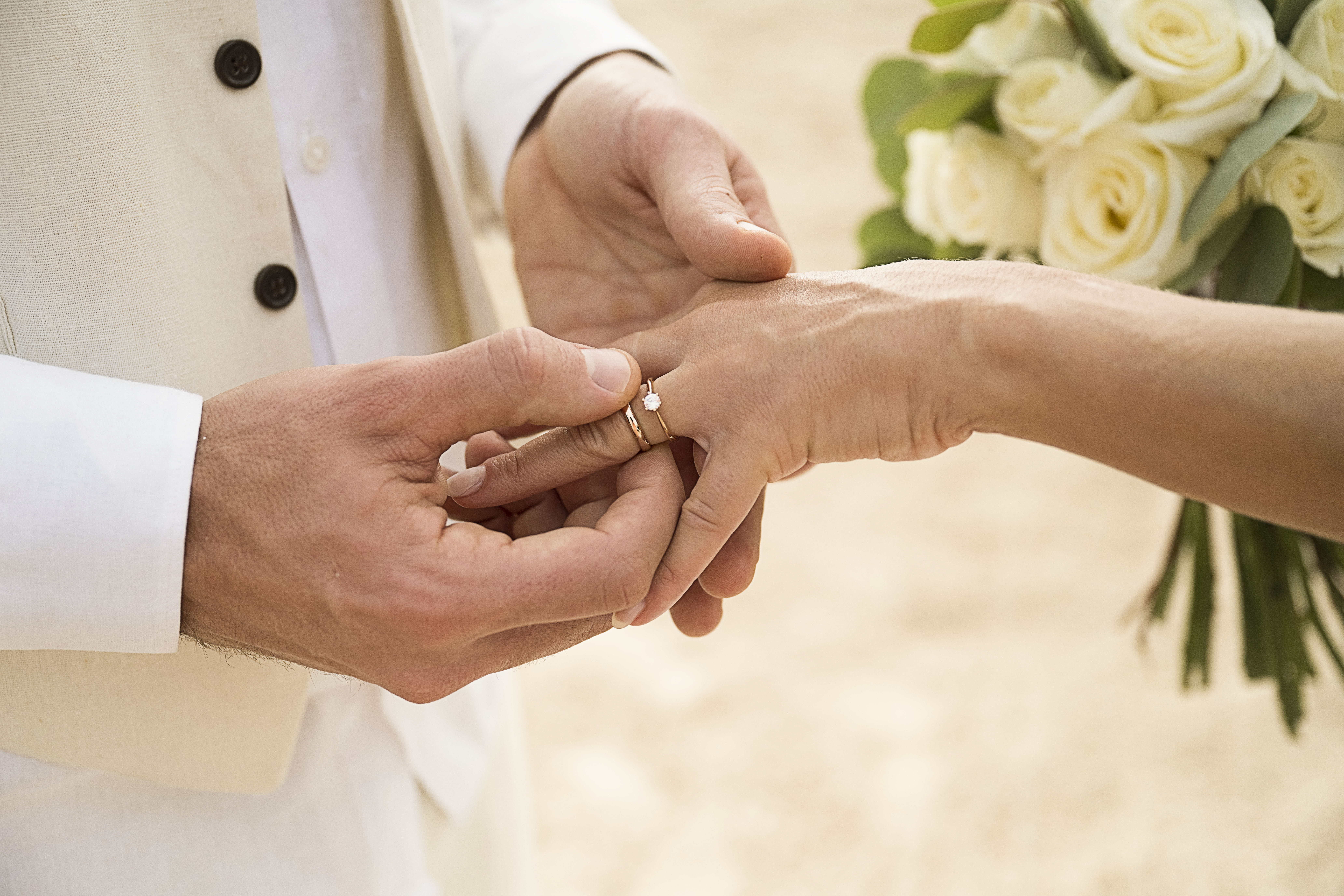 Groom placing wedding ring on bride's finger, white rose bouquet.